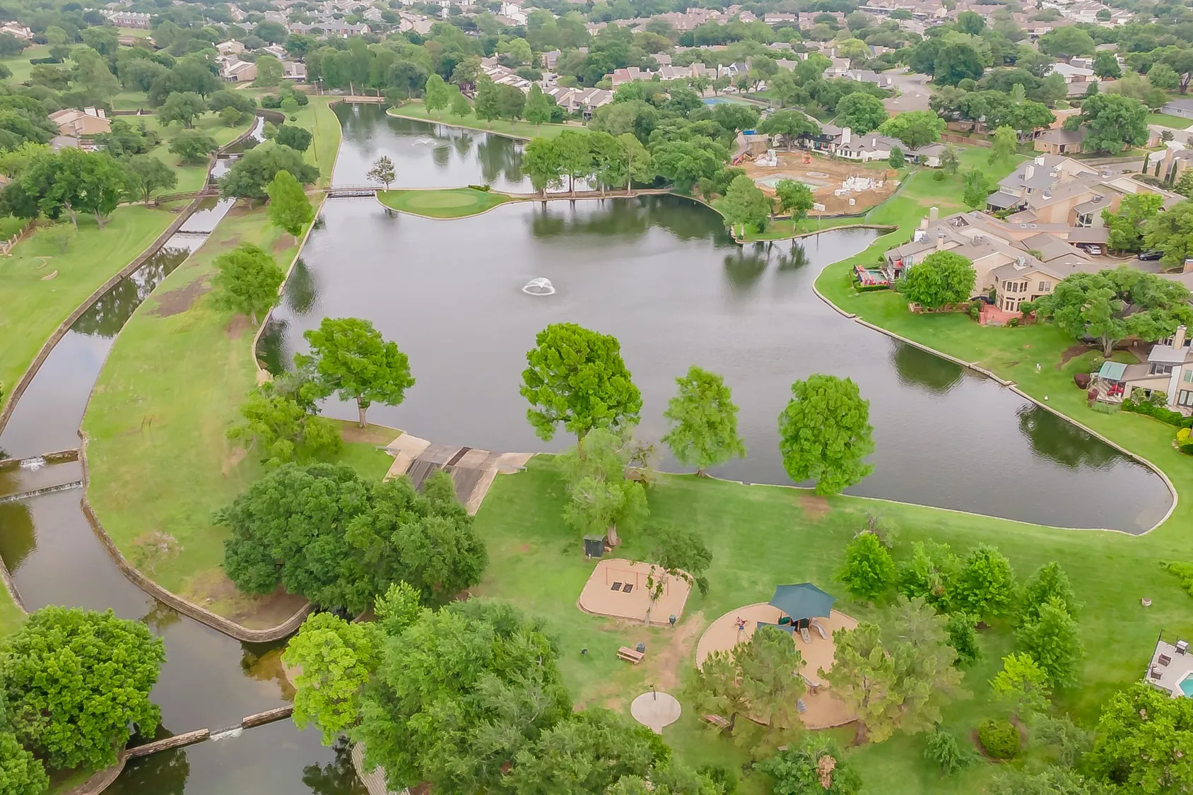 Expansive community lake with a central fountain, surrounded by lush green spaces and mature trees
