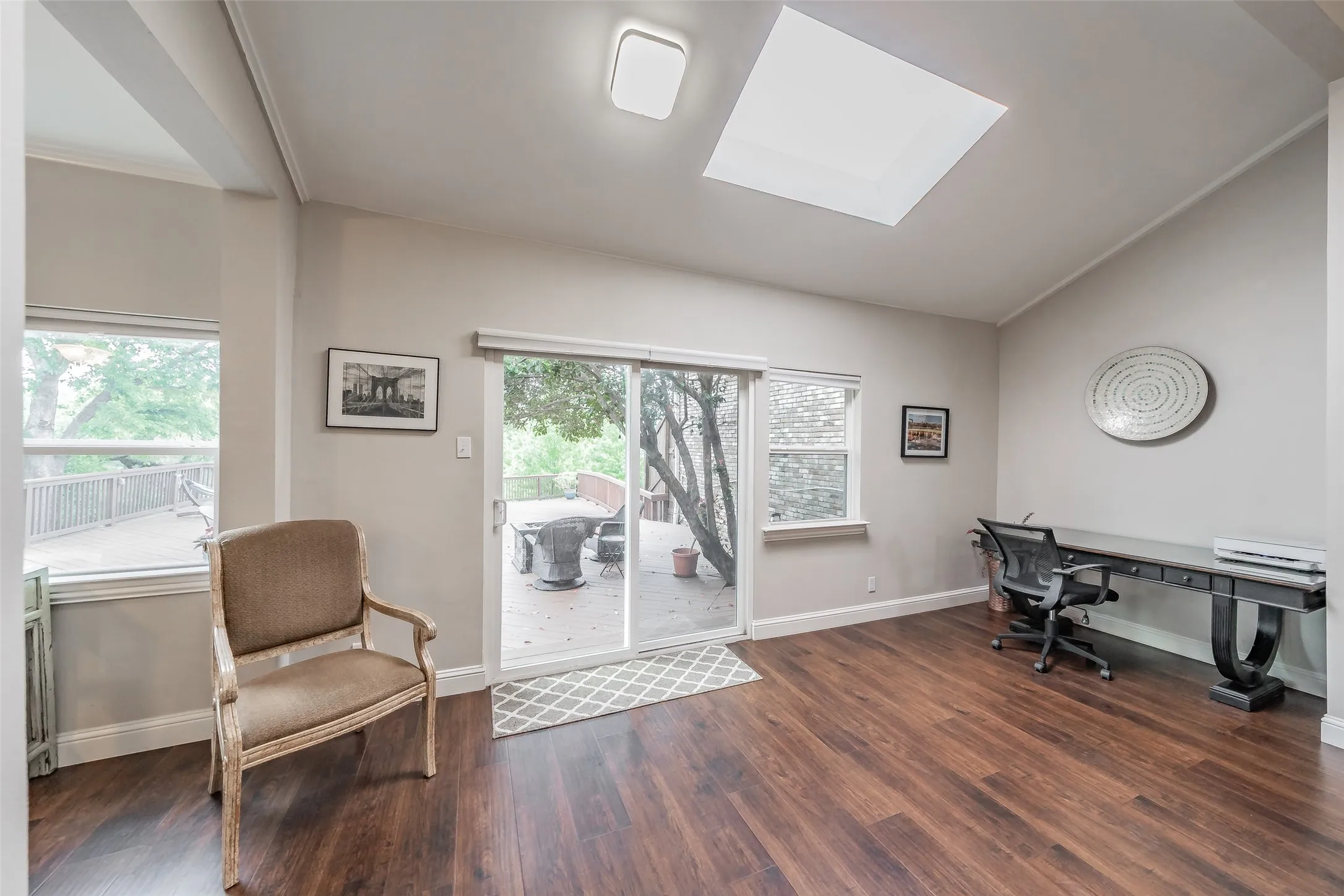 Spacious interior room featuring wood-finish flooring, a vaulted ceiling, and a skylight