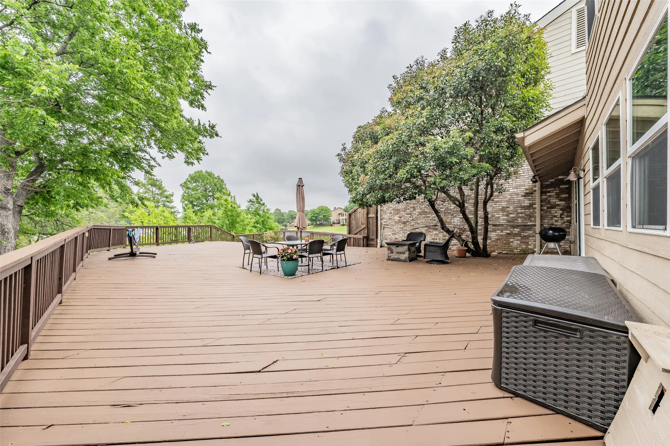 Expansive outdoor wood-finish deck with railing and mature trees
