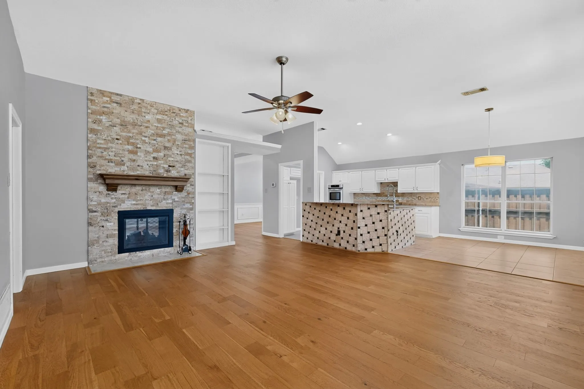 Open-concept living area featuring wood-finish flooring and a stone-clad fireplace with a wood mantle