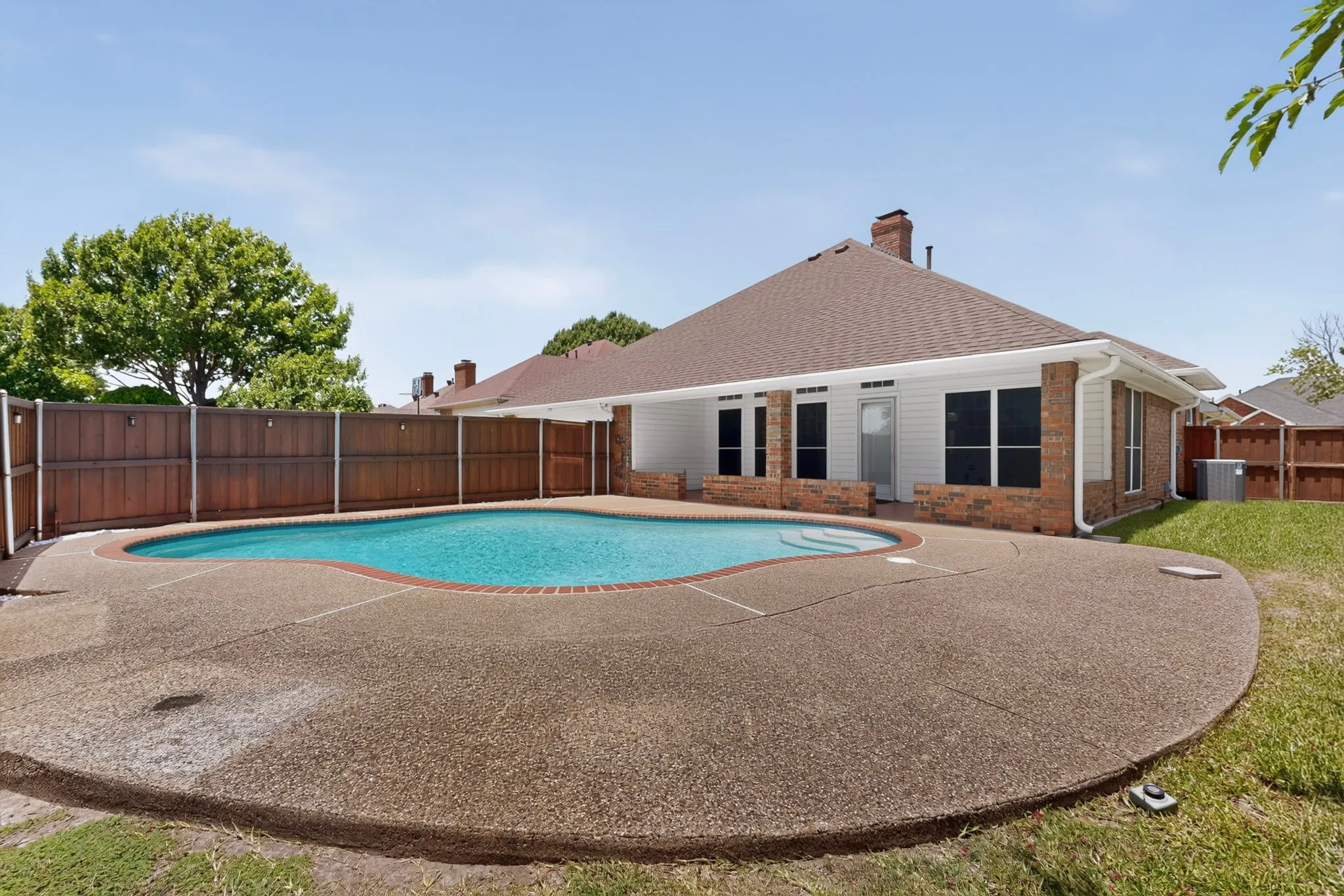 Expansive backyard featuring a kidney-shaped swimming pool with concrete decking
