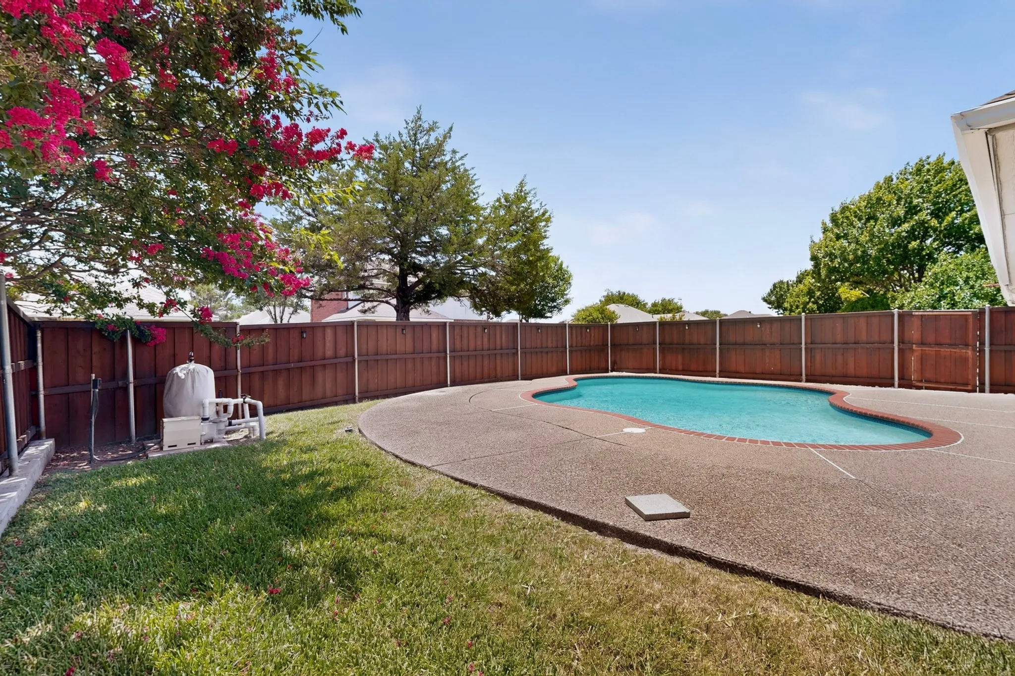 Curved swimming pool with an exposed aggregate concrete deck and perimeter fencing