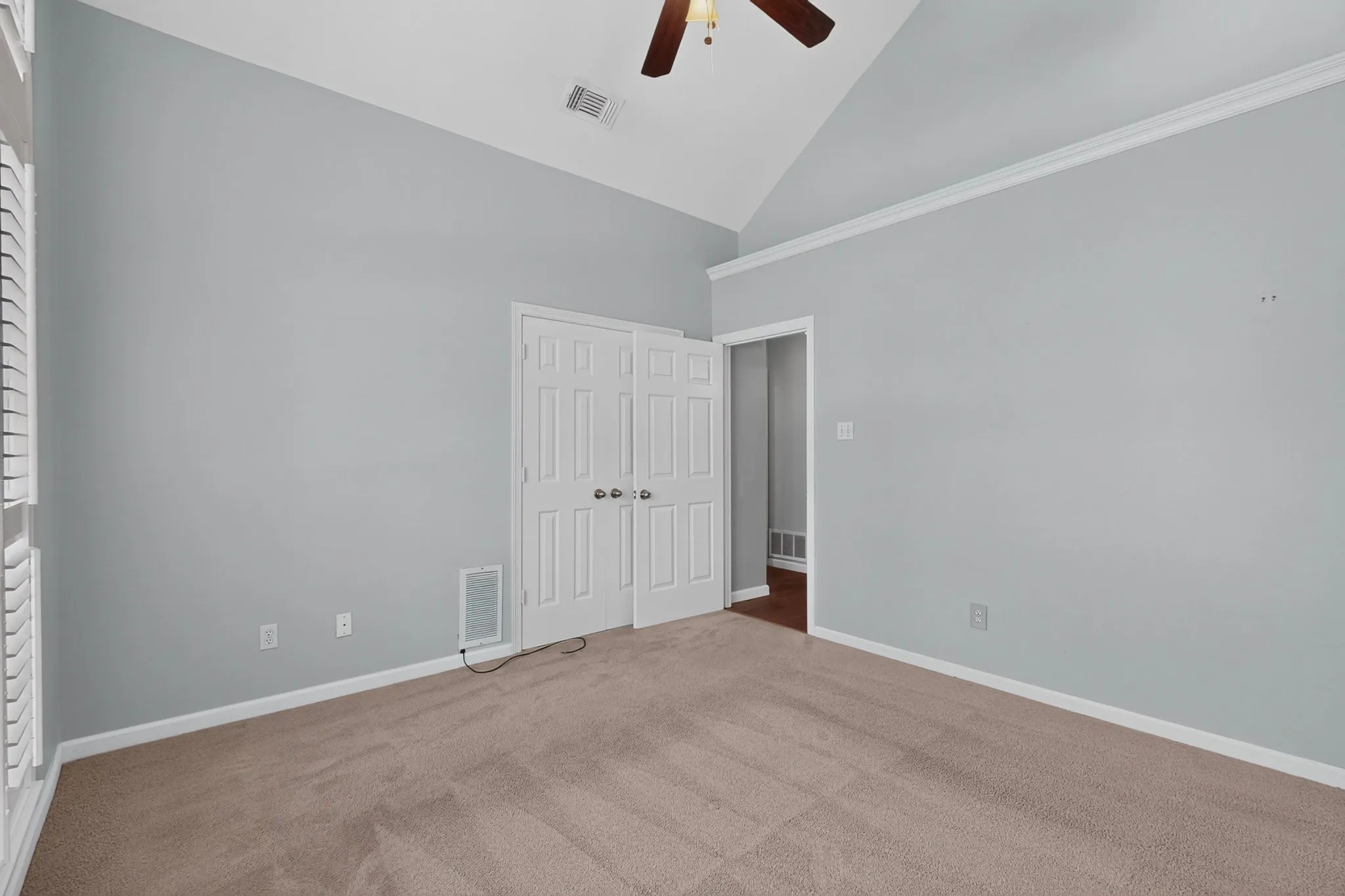 Room featuring a vaulted ceiling with a ceiling fan, light-colored carpeting, white baseboards, and a white crown molding accent