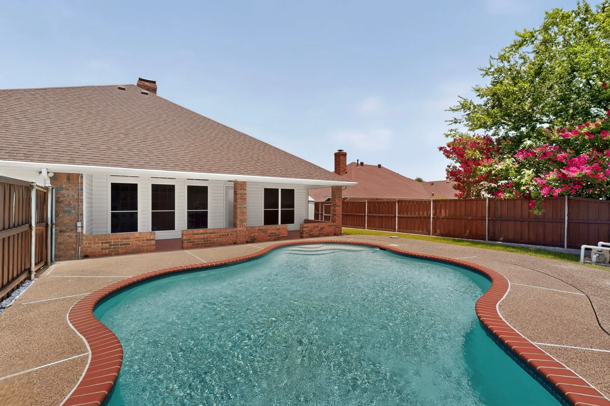 Freeform swimming pool with a textured concrete deck and brick coping