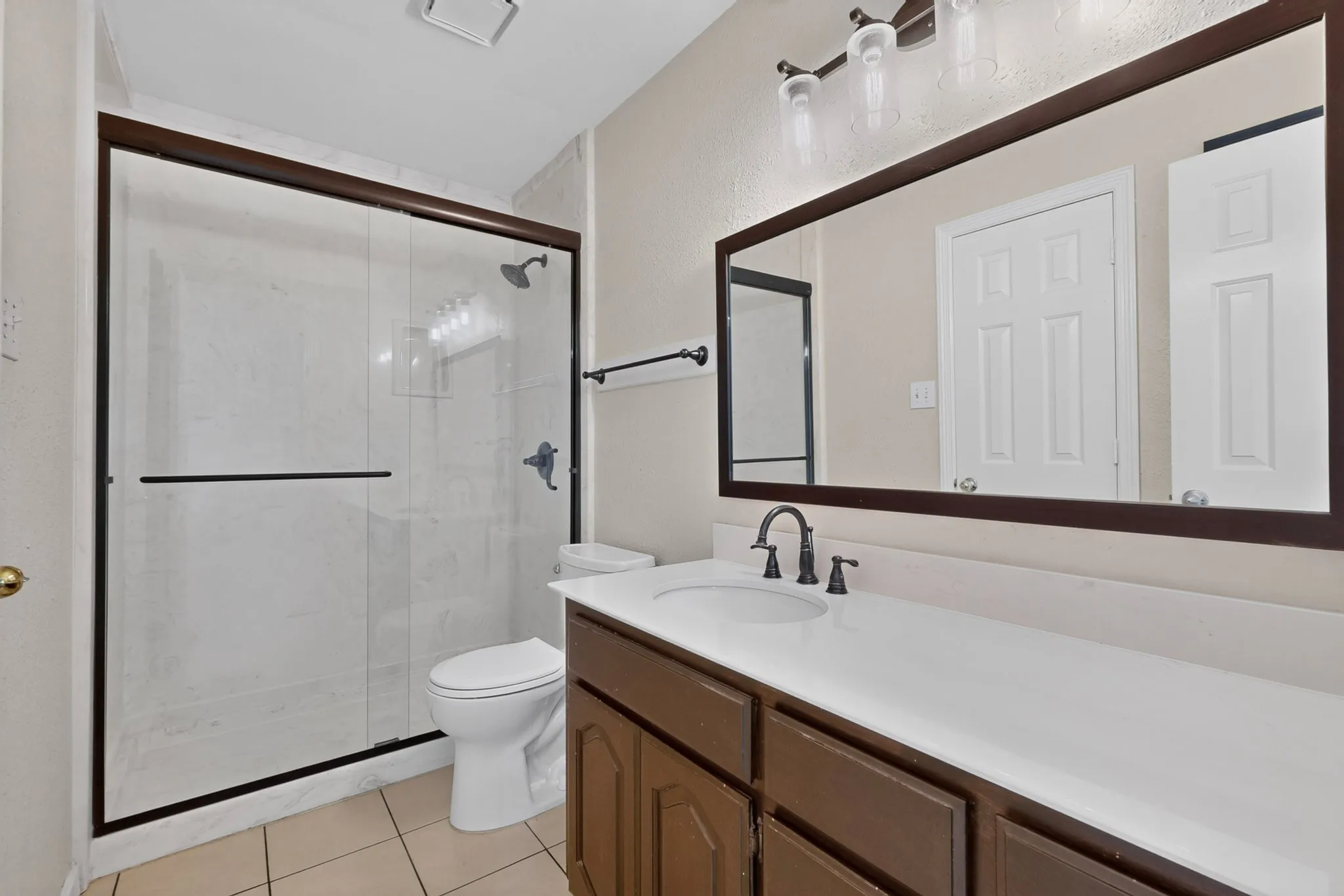 Full bathroom featuring a glass-enclosed shower, a vanity with a white countertop and dark cabinetry, a framed mirror, and tile flooring