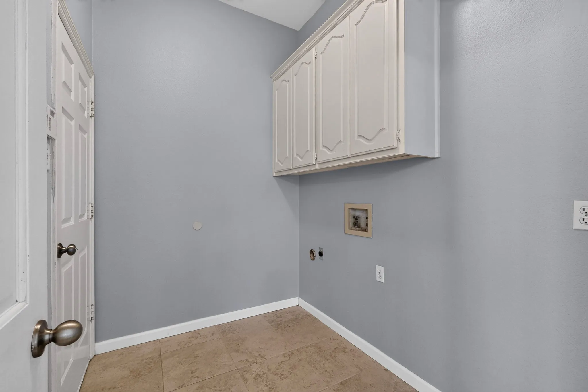 Laundry area featuring overhead cabinetry, utility connections, tile flooring, and a paneled door with bronze hardware