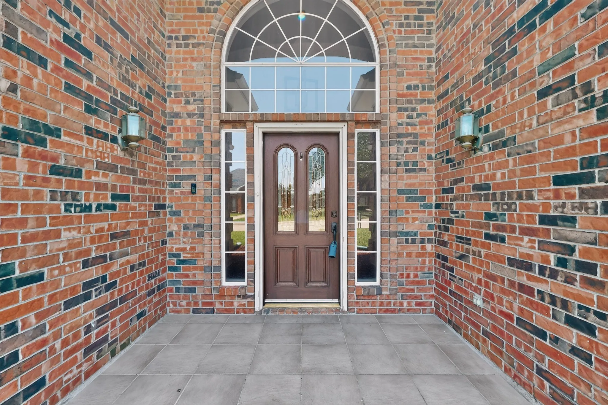 Brick exterior facade with a prominent arched transom window over a solid wood entry door