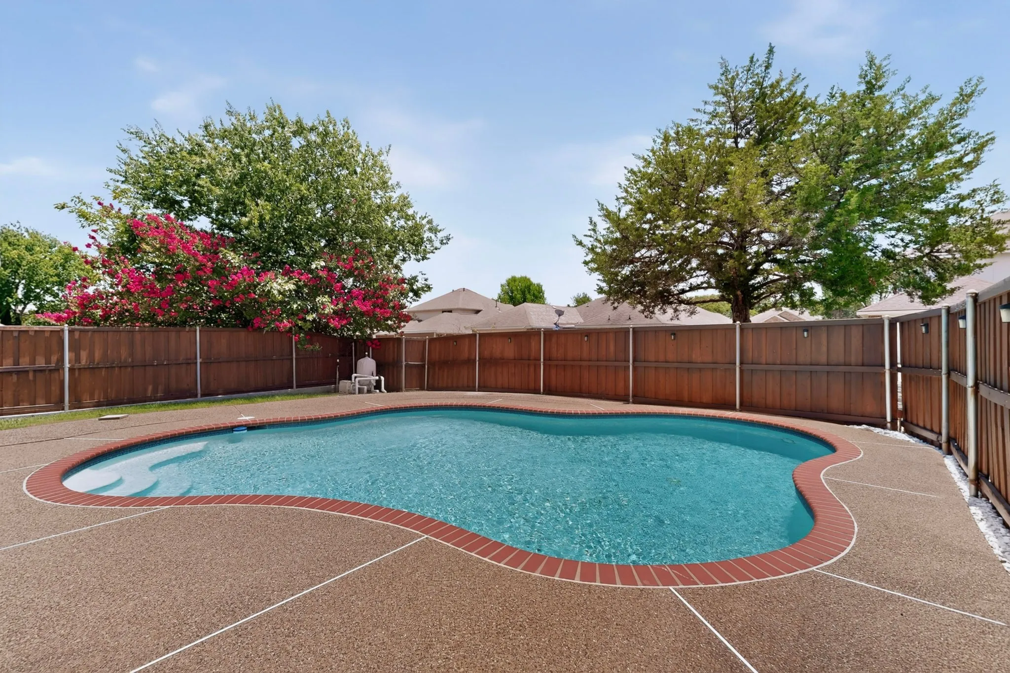 Freeform swimming pool featuring a brick coping and an exposed aggregate deck