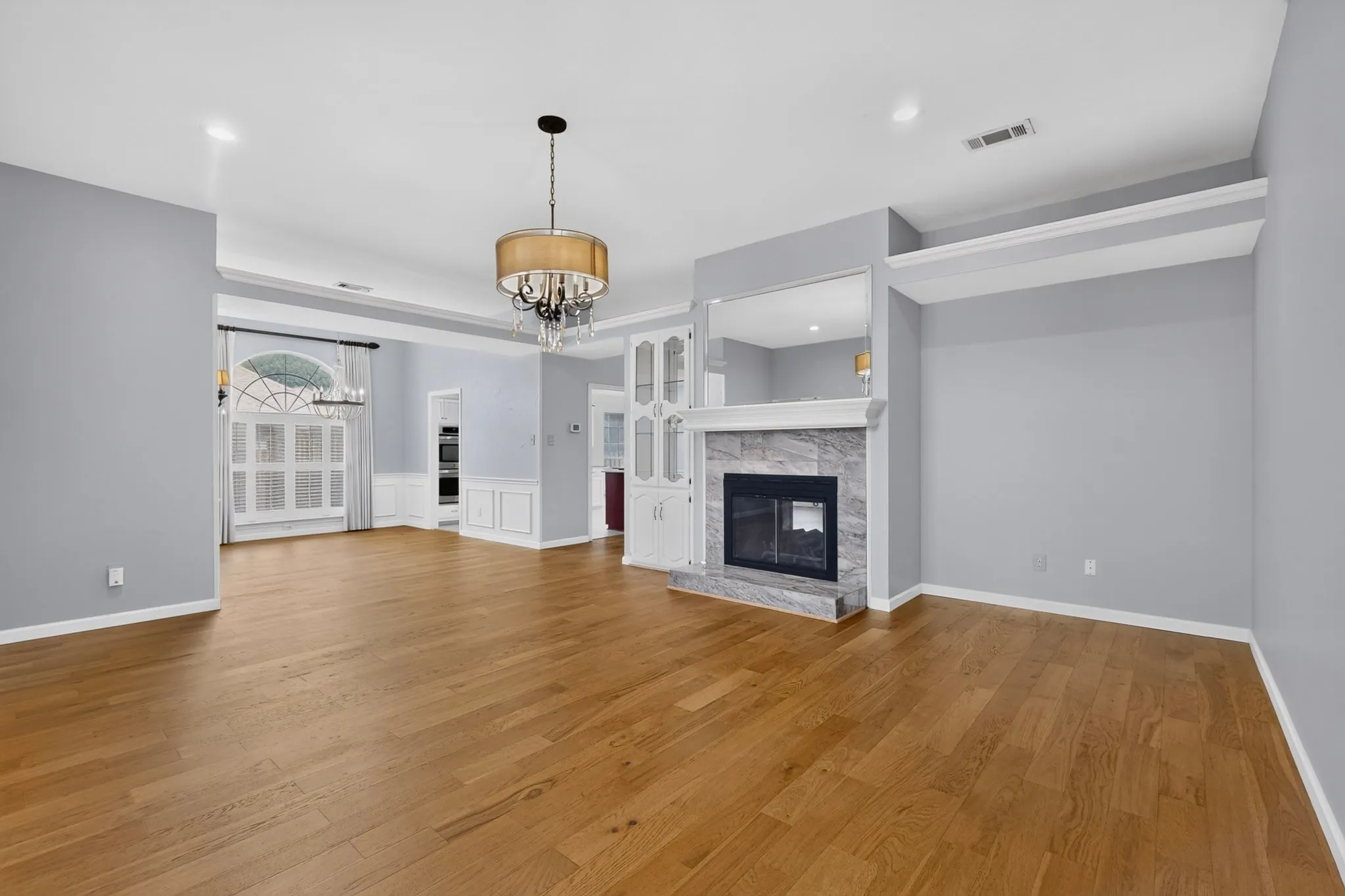 Expansive room featuring wood-finish flooring, a contemporary chandelier, and a fireplace with a stone surround