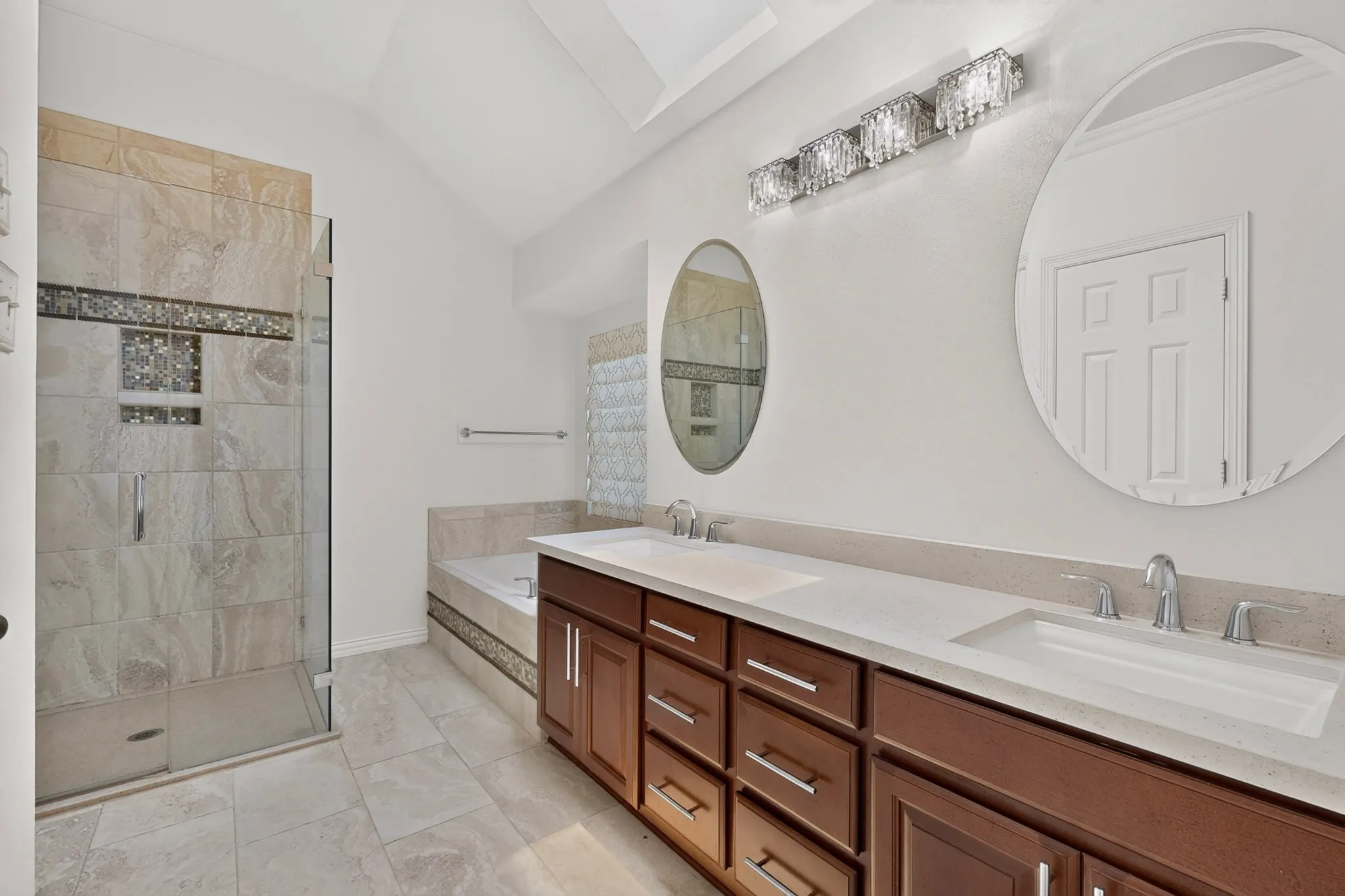 Vaulted ceiling bathroom featuring a double vanity with stone countertops, a glass-enclosed shower with tile surround and decorative accents, a built-in bathtub with tile surround, and polished chrome fixtures