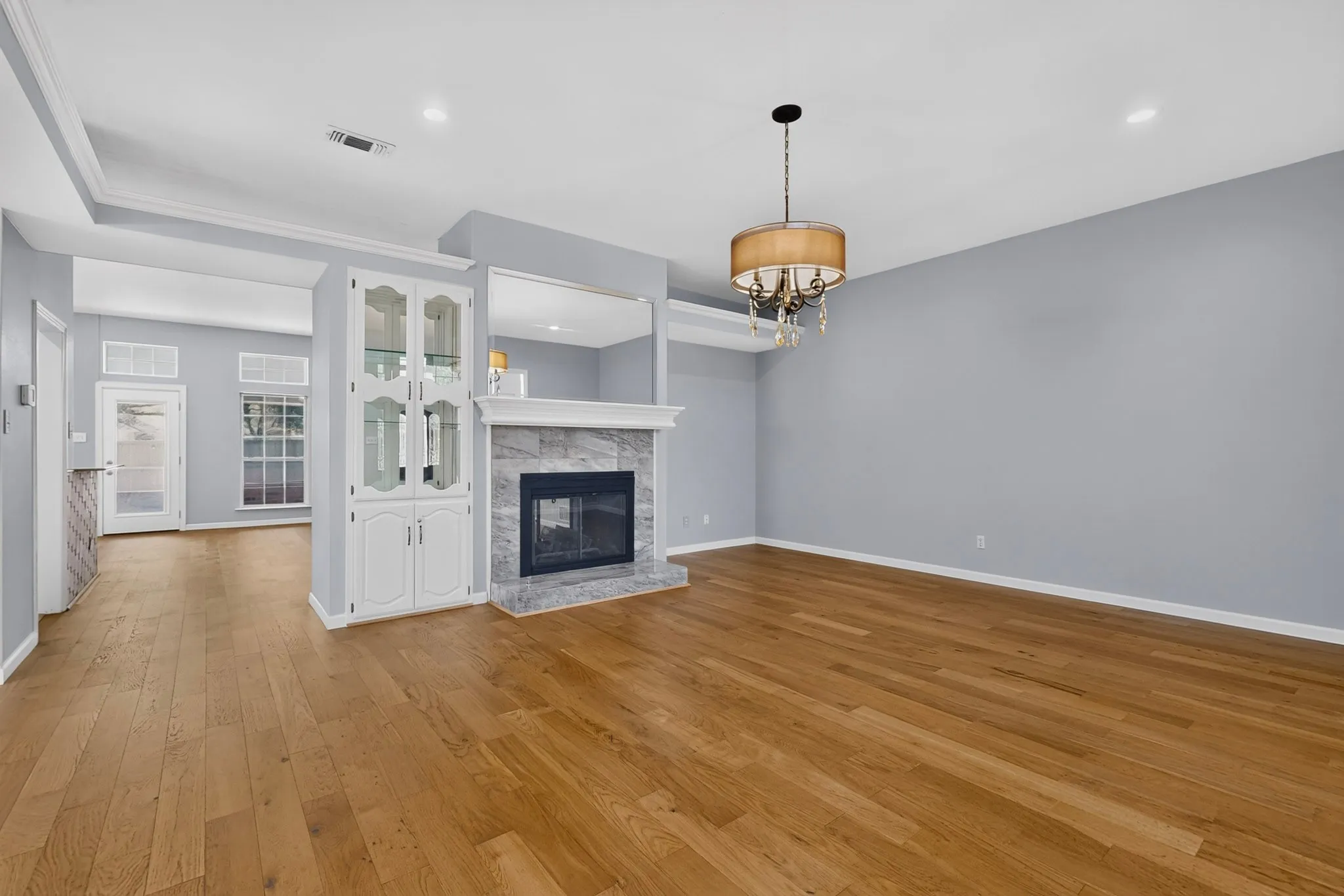 Expansive living area featuring wood-finish flooring, a contemporary fireplace with a stone surround, a built-in display cabinet, a decorative chandelier, and tray ceilings