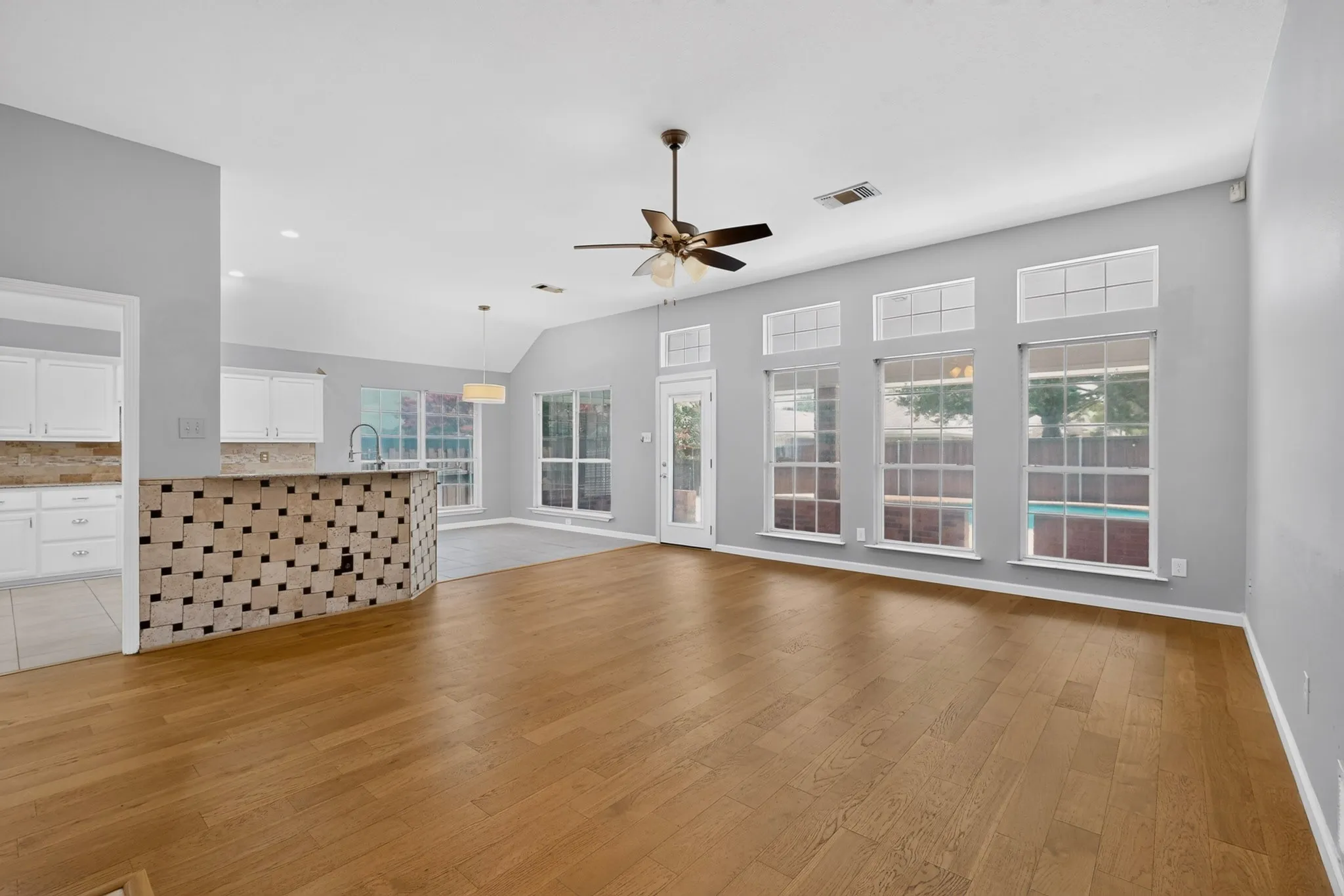 Spacious living area featuring wood-finish flooring, vaulted ceilings, and a ceiling fan