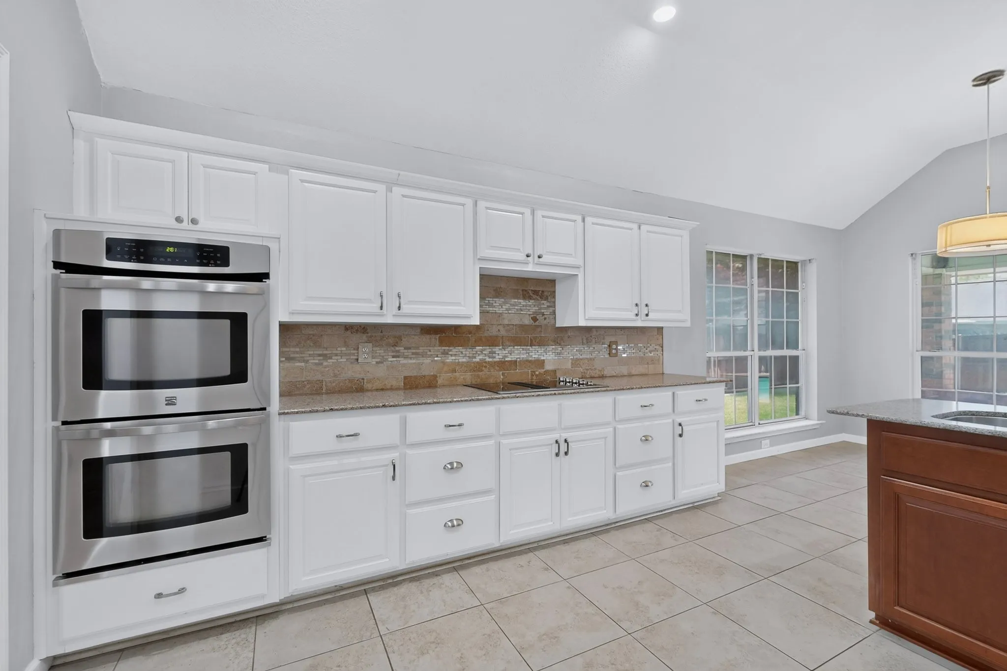 Kitchen featuring white cabinetry, stainless steel double ovens, a stone-finish backsplash, speckled countertops, and tile flooring