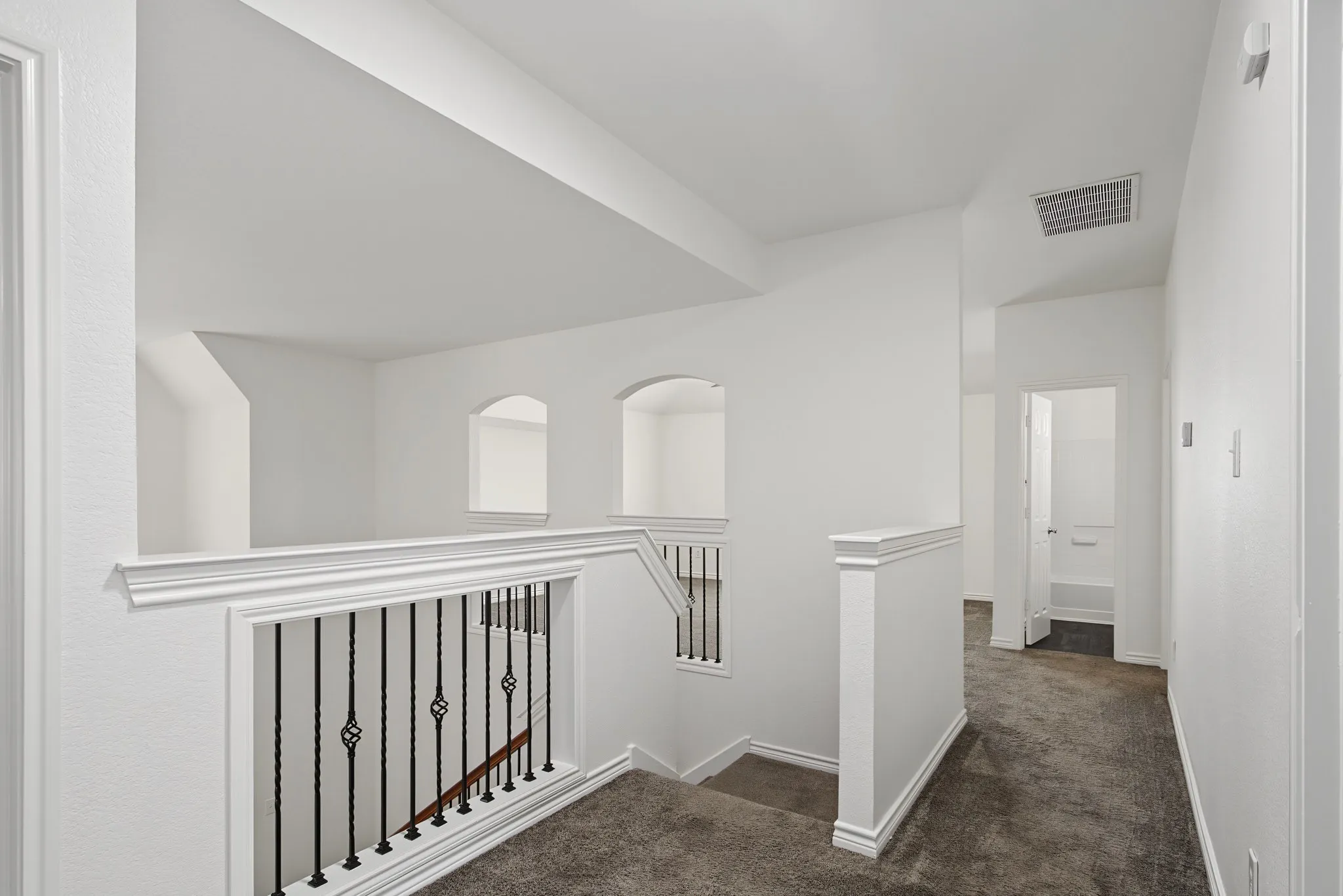 Carpeted hallway featuring a staircase with wrought iron balusters, white newel posts, and wood-finish handrails