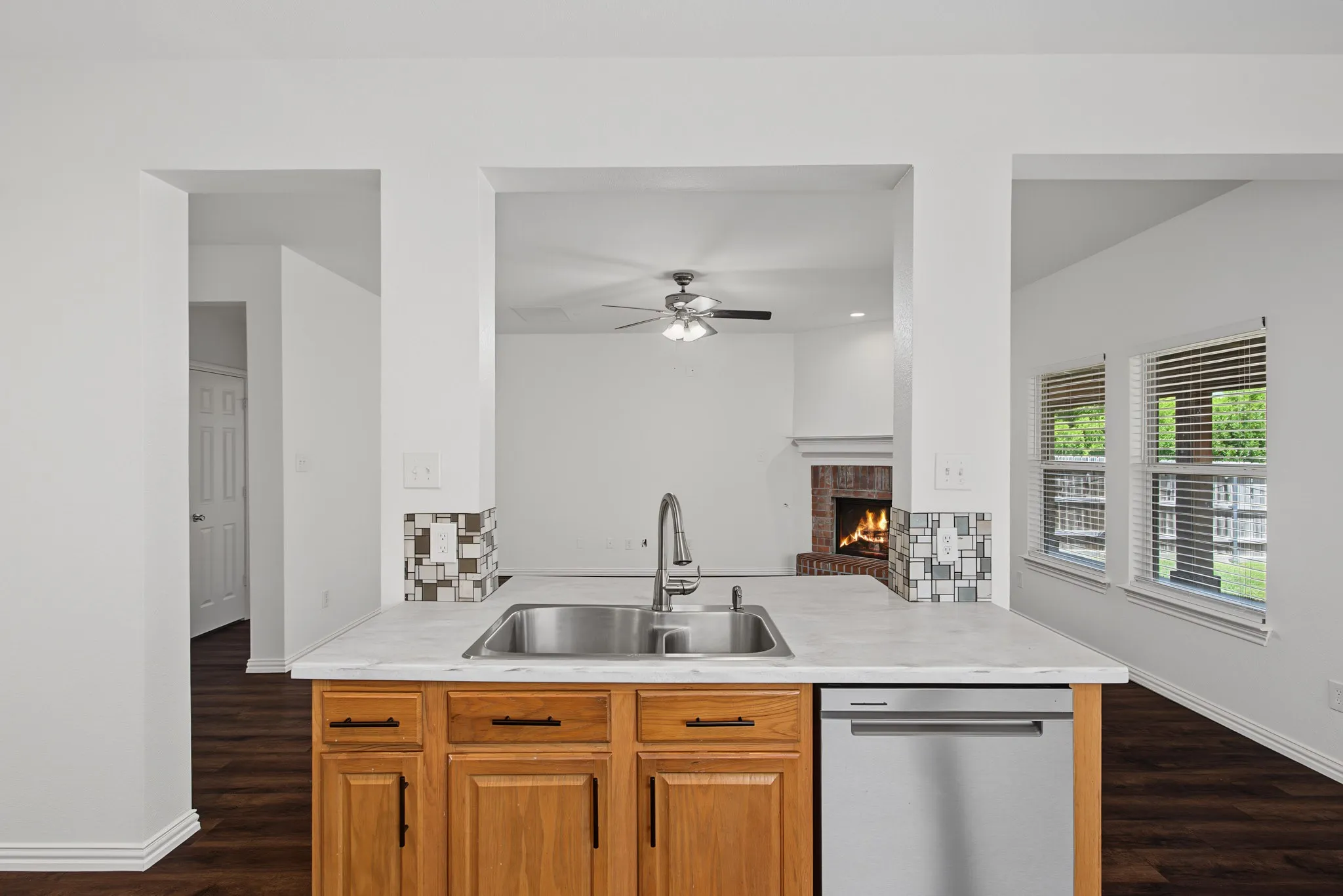 Kitchen island with an undermount stainless steel sink, a modern pull-down faucet, light-toned countertops, and wood-finish cabinetry