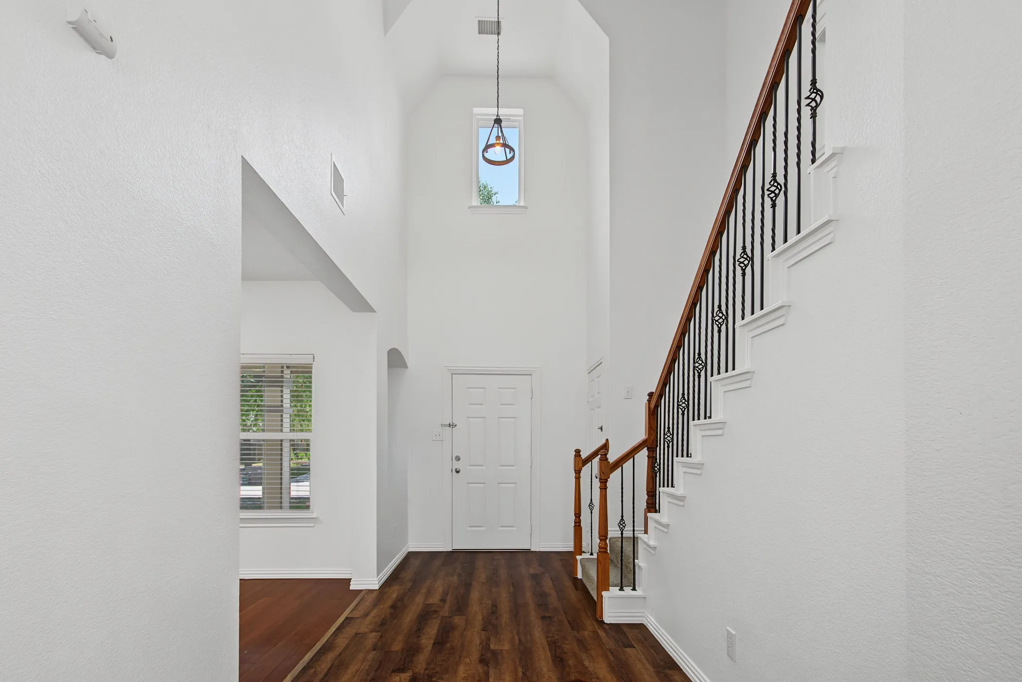 Two-story foyer featuring wood-finish flooring, a white paneled door, and a staircase with an ornamental wrought iron railing and wood handrail