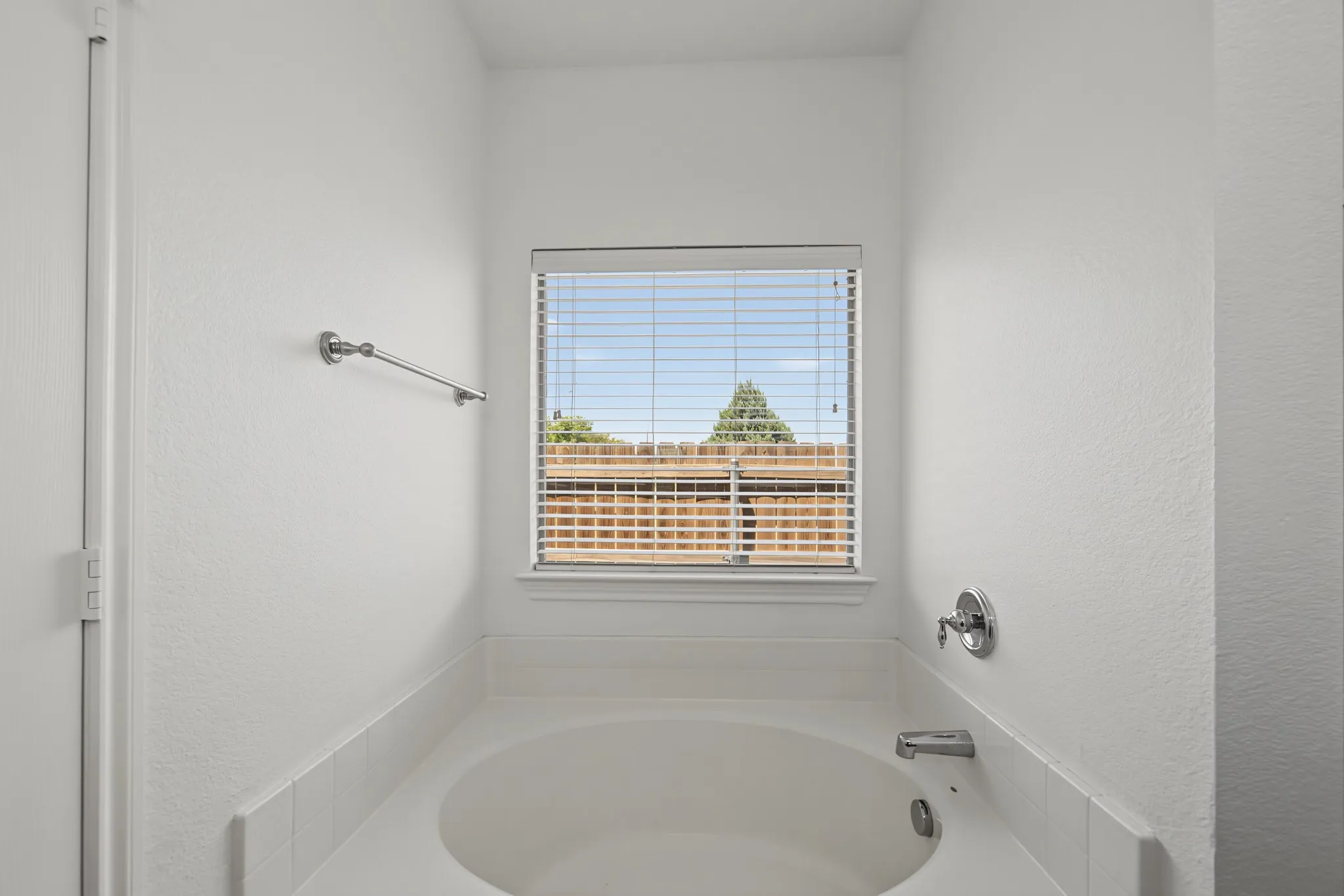 Alcove bathtub featuring a white tile surround, privacy blinds, chrome fixtures, and a wall-mounted towel bar
