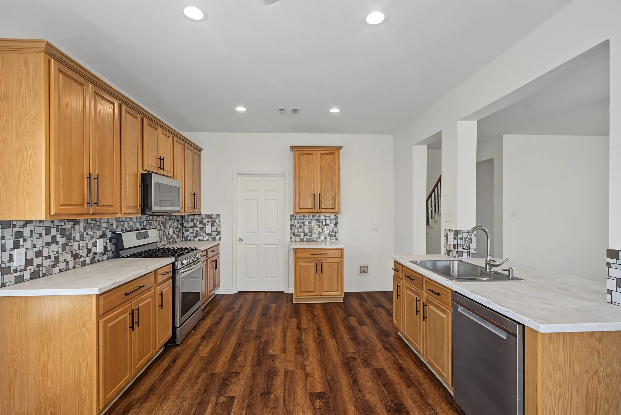 Bright kitchen featuring wood-finish flooring, light-colored cabinetry, a mosaic tile backsplash, stainless steel appliances, and recessed lighting
