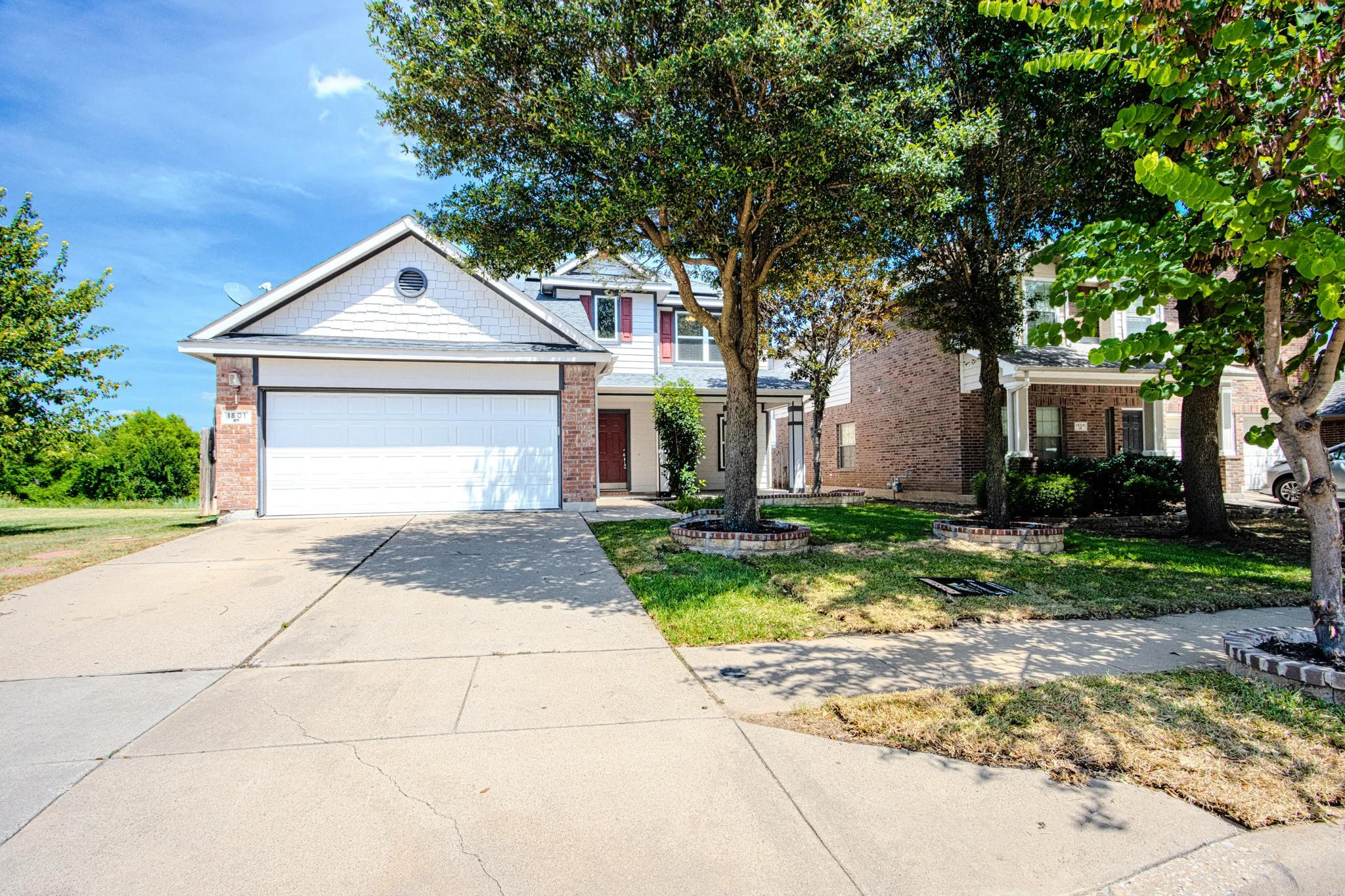 Two-story residence featuring a brick facade with white siding and a prominent two-car garage