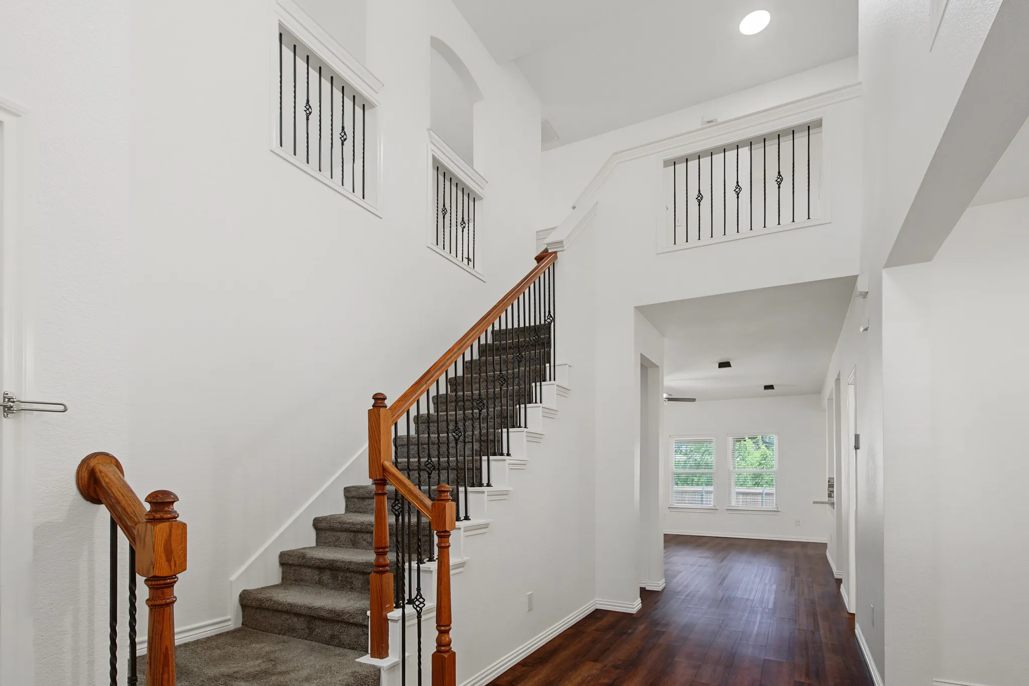 Two-story foyer featuring a carpeted staircase with wood handrails and wrought iron balusters