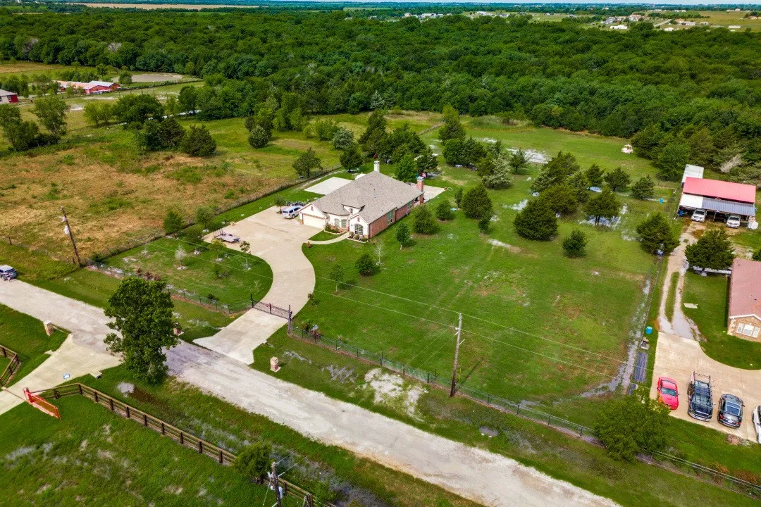Expansive property featuring a brick residence with a gabled roofline, a lengthy paved driveway, and mature landscaping