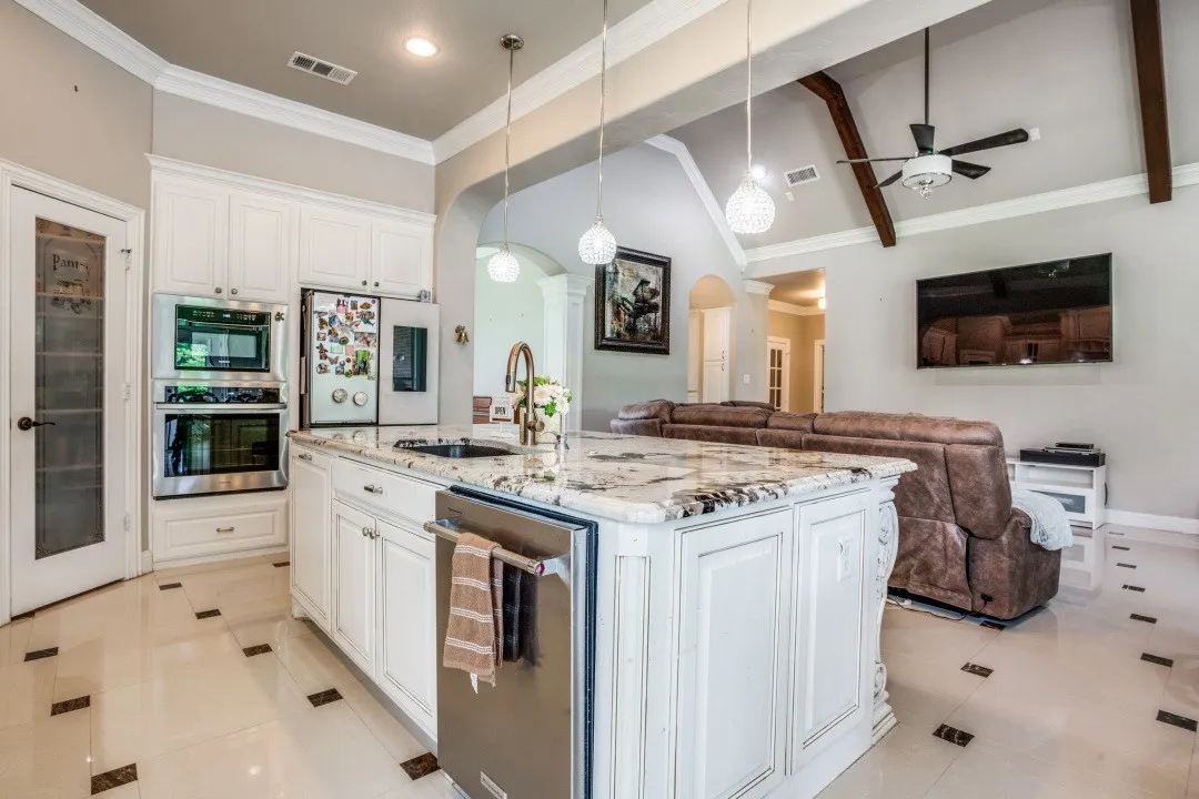 Gourmet kitchen featuring a large island with a stone countertop, white cabinetry, stainless steel appliances, and polished tile flooring with dark accent squares
