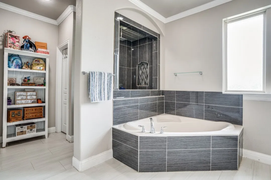 Corner soaking tub featuring dark gray tiled surround