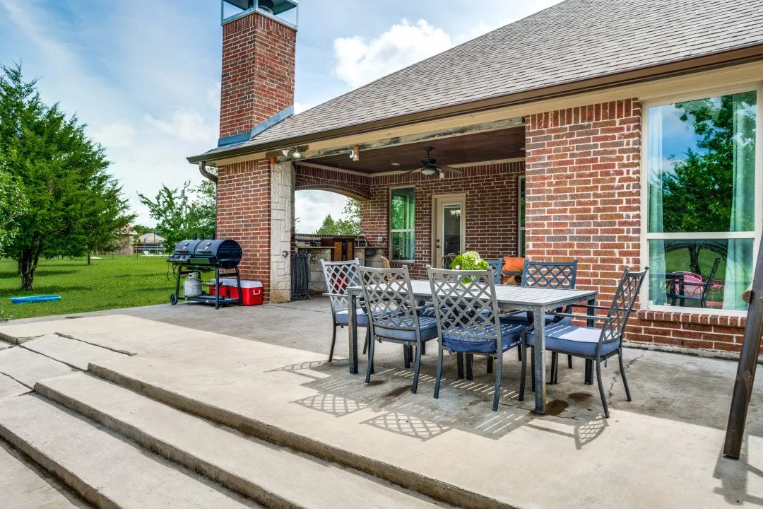 Expansive outdoor patio with a covered area, brick exterior, and a built-in outdoor kitchen with stone accents