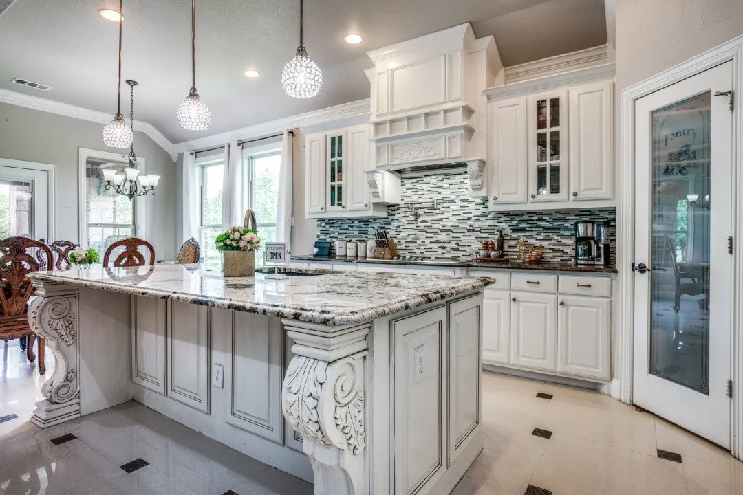 Kitchen featuring a large island with granite countertops and decorative corbels, white cabinetry, a mosaic tile backsplash, and recessed lighting