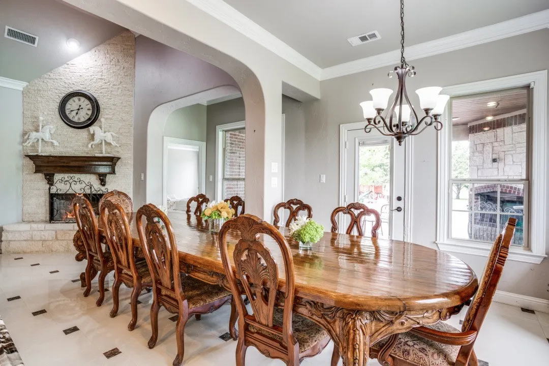 Formal dining area featuring a stone fireplace with a wood mantel, crown molding, arched entryways, and tile flooring with dark accent squares