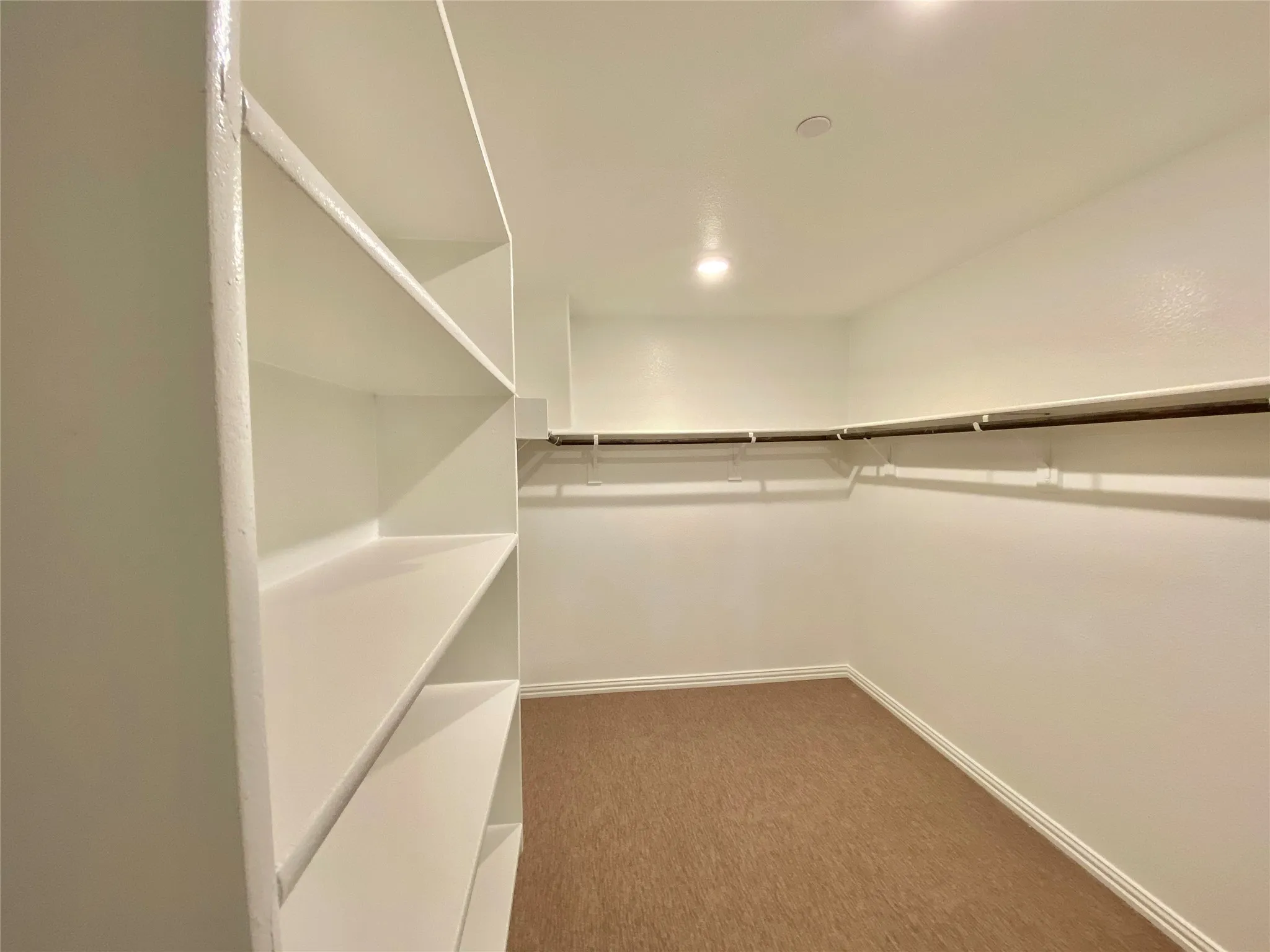 Spacious walk-in closet featuring built-in shelving, hanging rods, recessed lighting, and carpet flooring