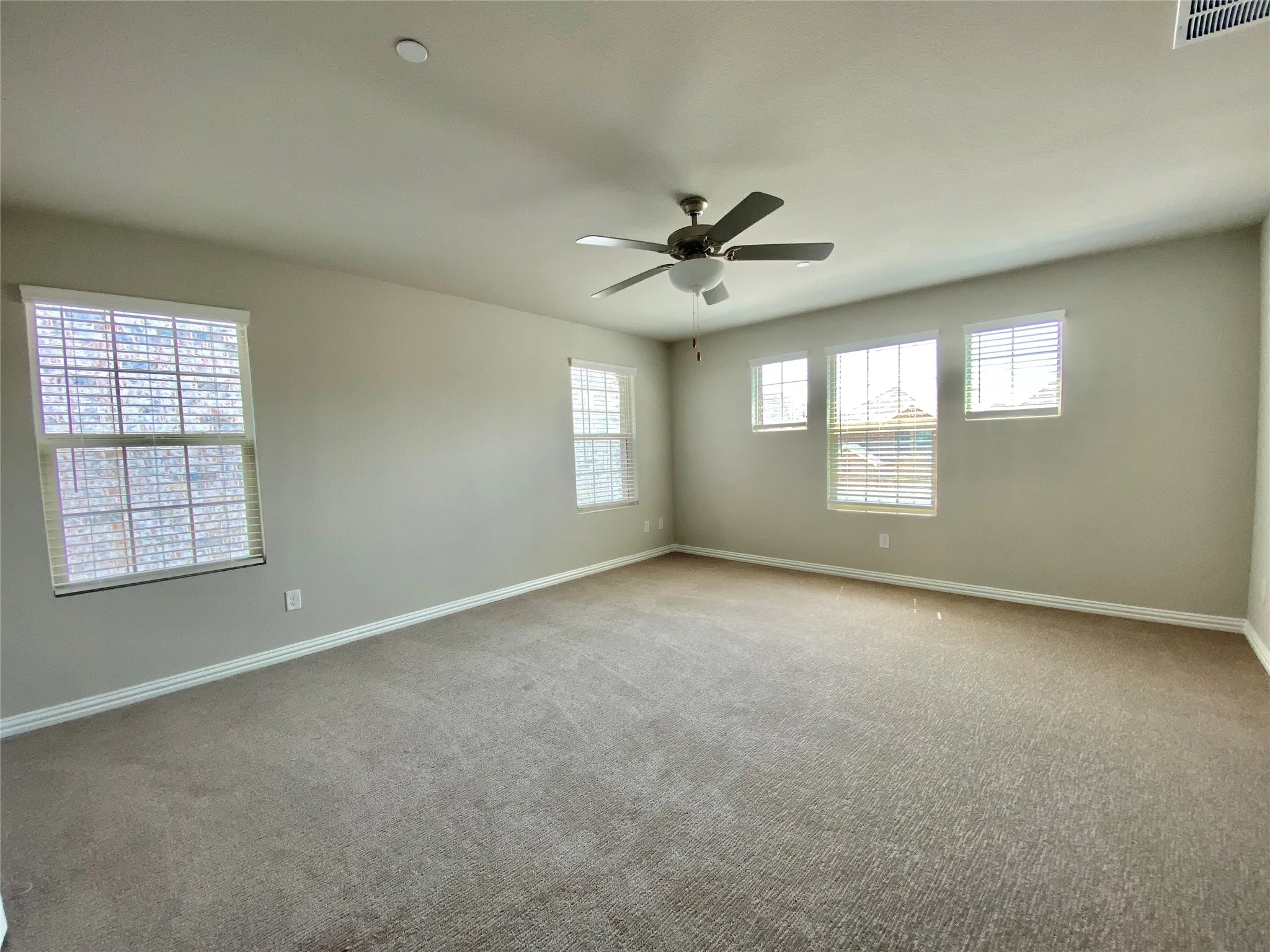 Spacious room featuring neutral carpeting, a ceiling fan with integrated lighting, multiple windows with blinds, and recessed lighting