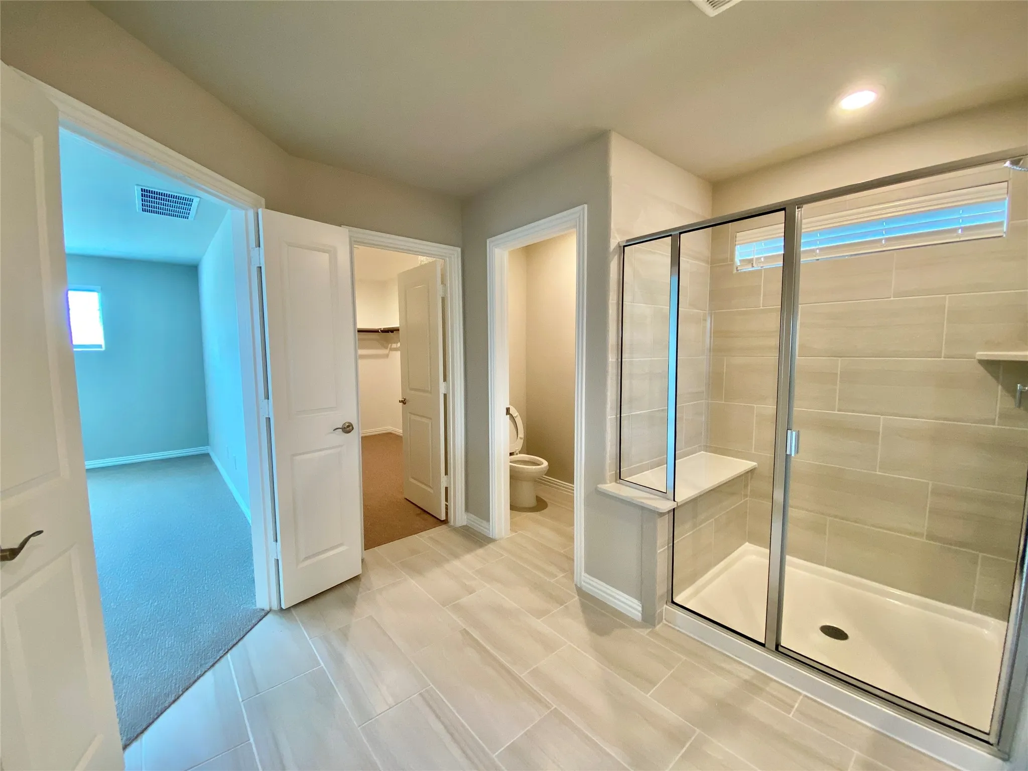 Spacious bathroom featuring large format tile flooring, a glass-enclosed shower with a built-in bench, and a tiled shower surround