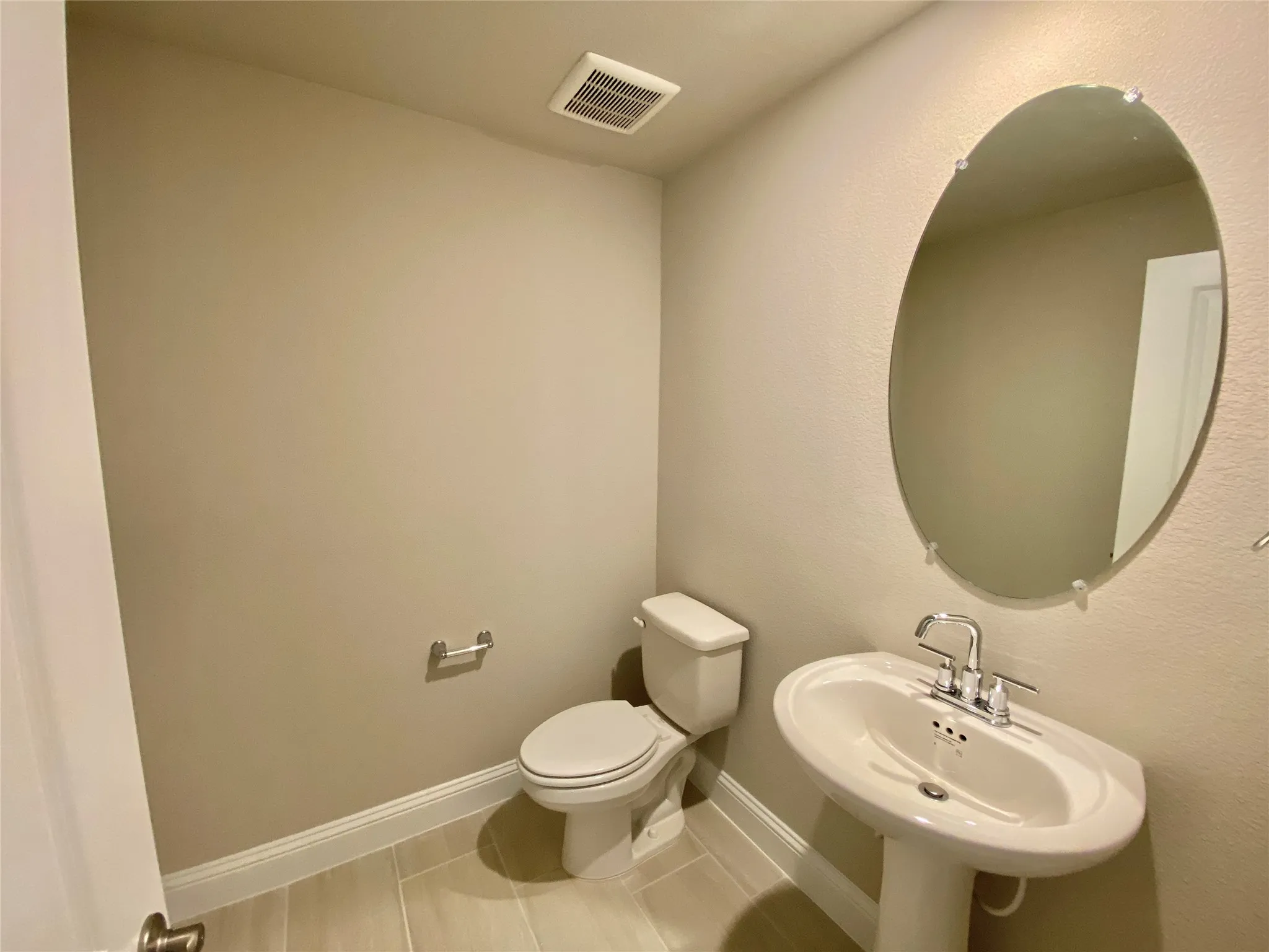 Pedestal sink with chrome fixtures and an oval wall mirror