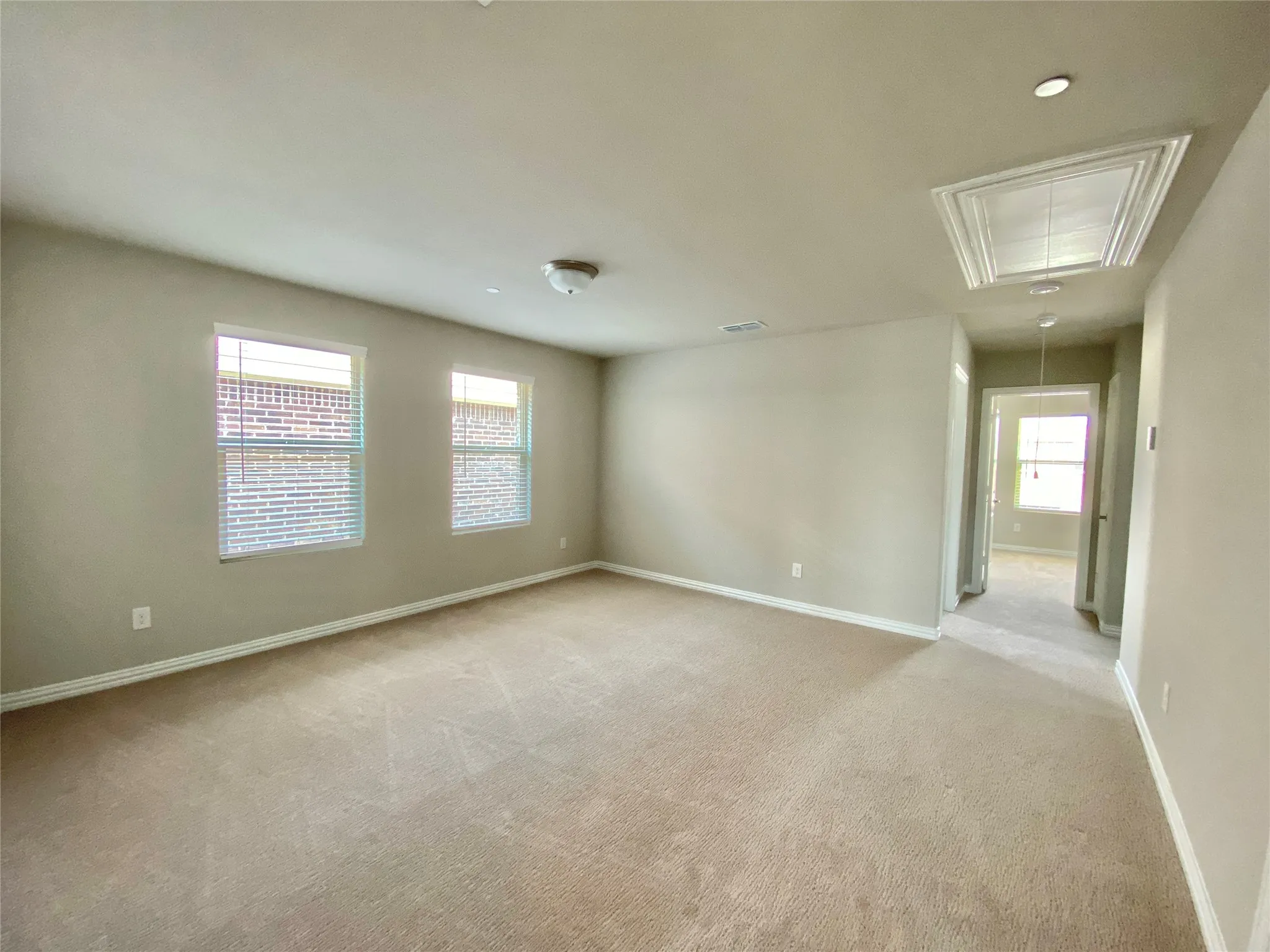 Spacious room featuring neutral carpeting, two large windows with blinds, light-toned wall paint, a flush-mount ceiling light, and recessed lighting