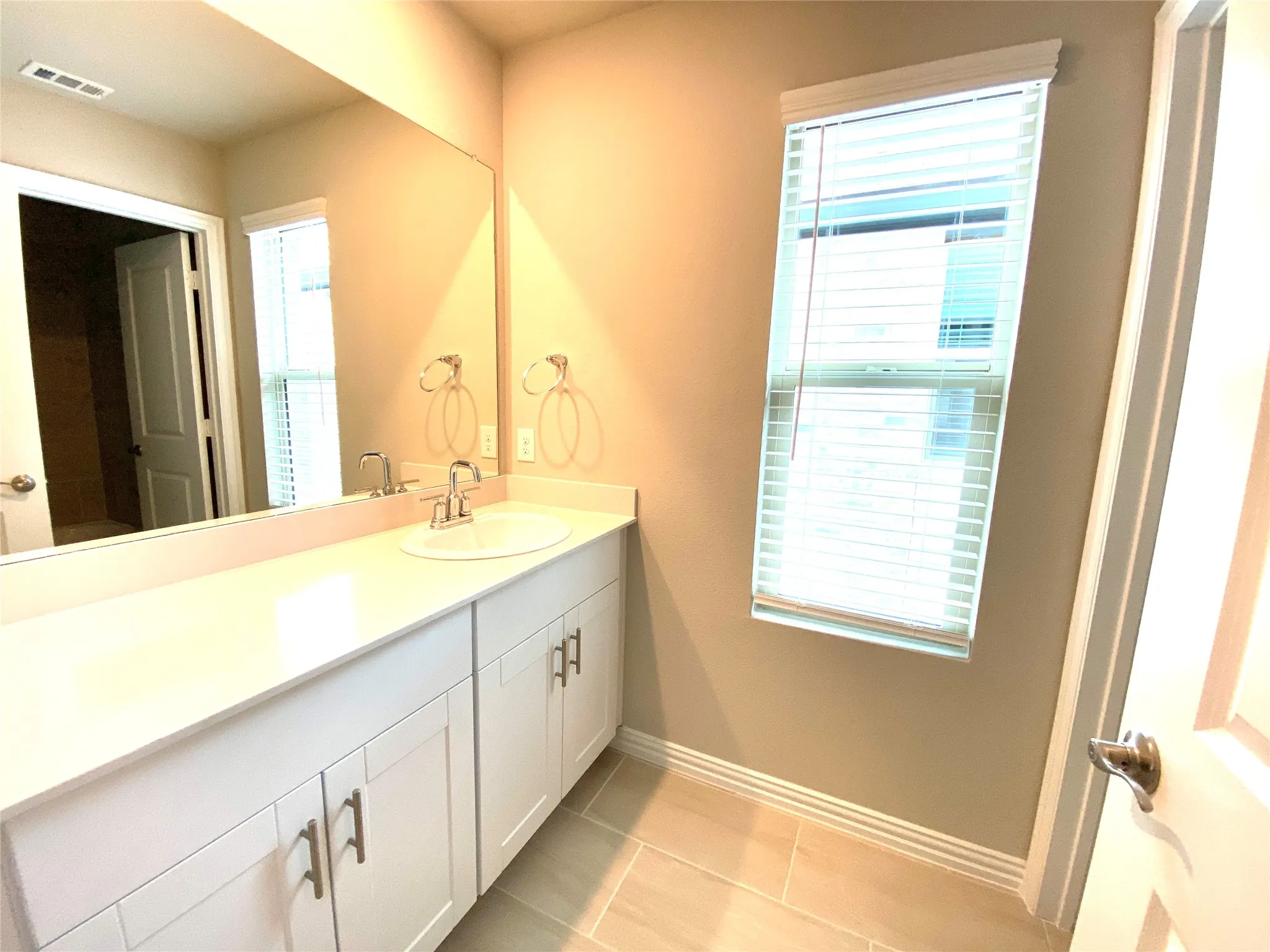 Bathroom vanity featuring a rectangular undermount sink, a wide mirror, and white shaker-style cabinetry with brushed nickel hardware