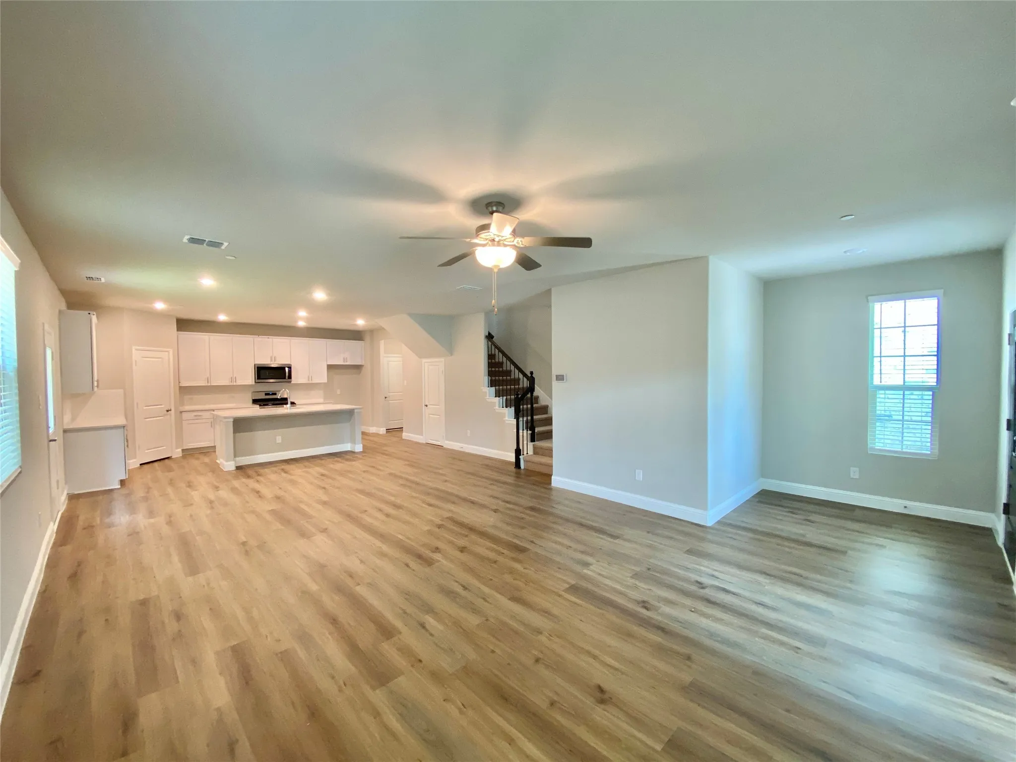 Open-concept living space featuring wood-finish flooring, recessed lighting, and a modern kitchen with white cabinetry and an island