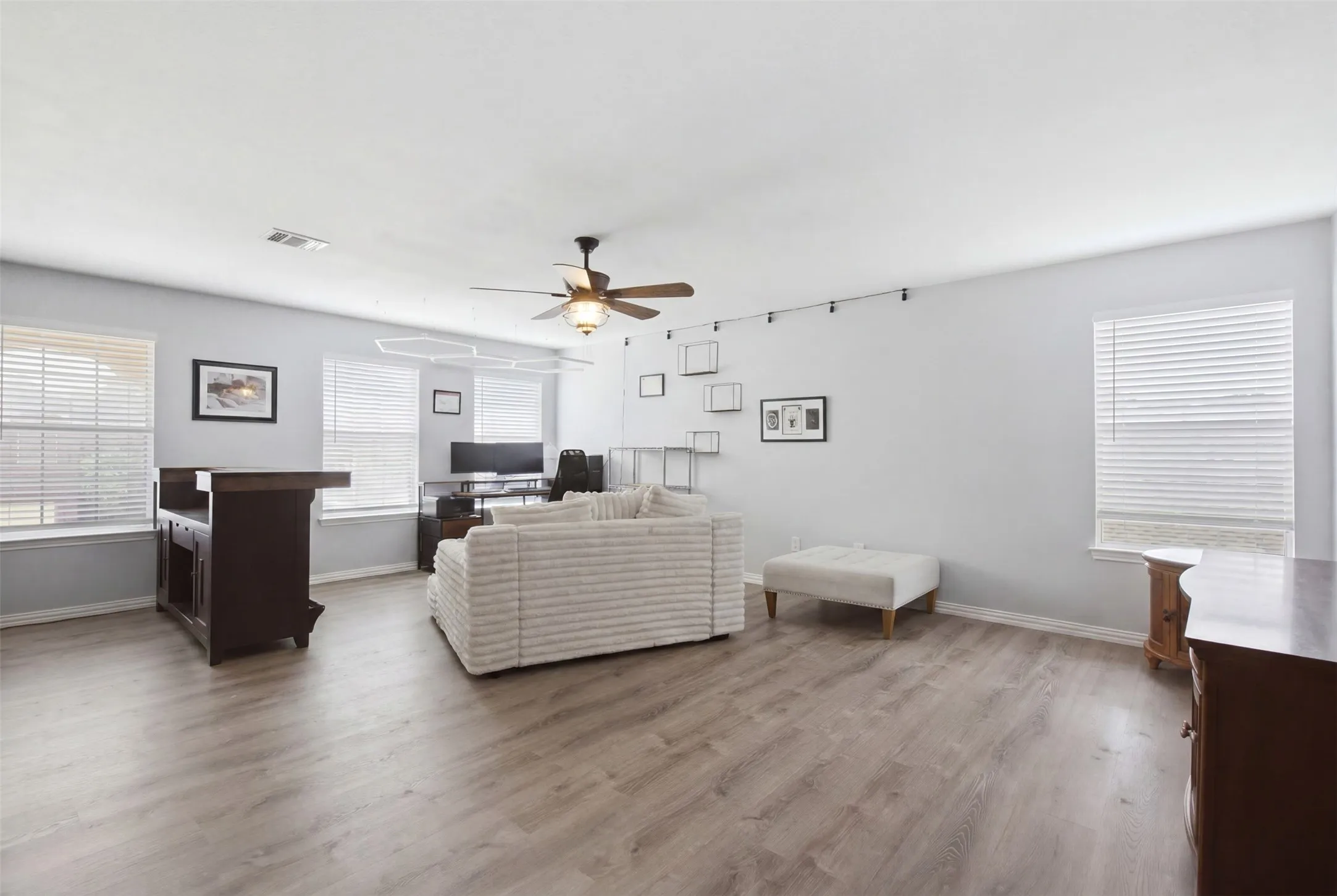 Spacious interior featuring wood-finish flooring, light gray wall tones, and multiple windows with blinds