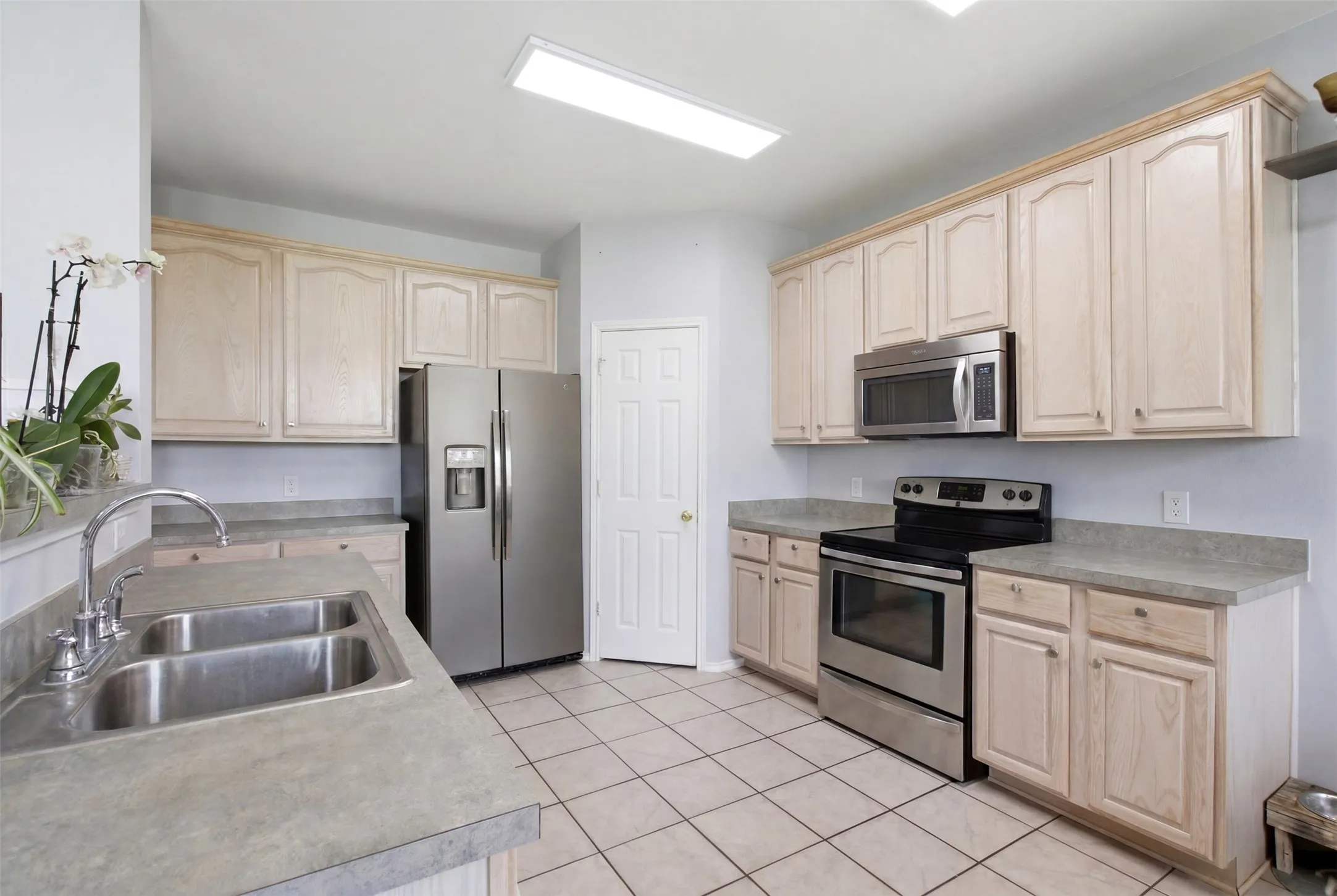 Kitchen featuring wood-finish cabinetry, stainless steel appliances, a dual basin sink, and tile flooring