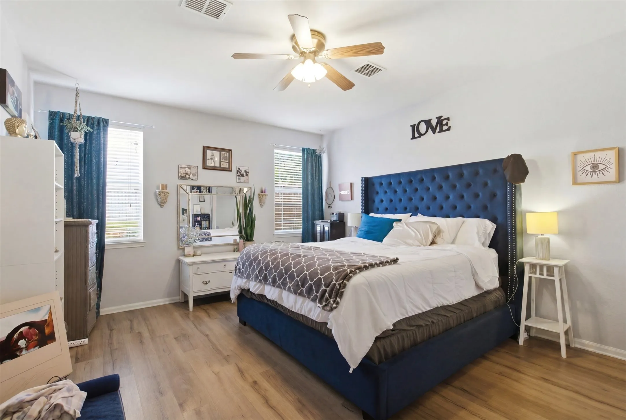 Bedroom featuring wood-finish flooring, two windows with blinds, a ceiling fan with integrated lighting, and light-toned walls