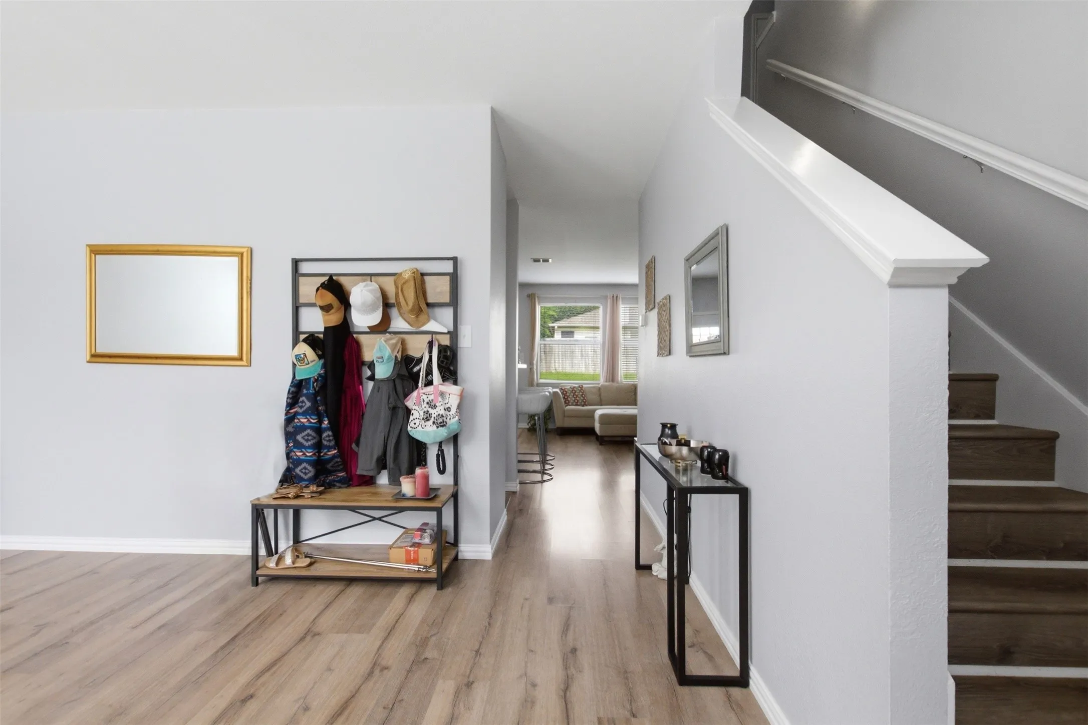 Bright entry hall featuring wood-finish flooring, light grey wall paint, a staircase with white risers and dark wood-finish treads, and a visible hallway extending to the back of the property