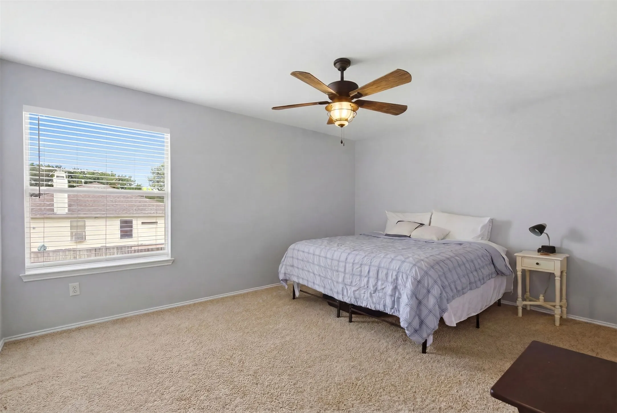 Carpeted bedroom featuring a ceiling fan with light fixture, large window with blinds, and light gray wall paint