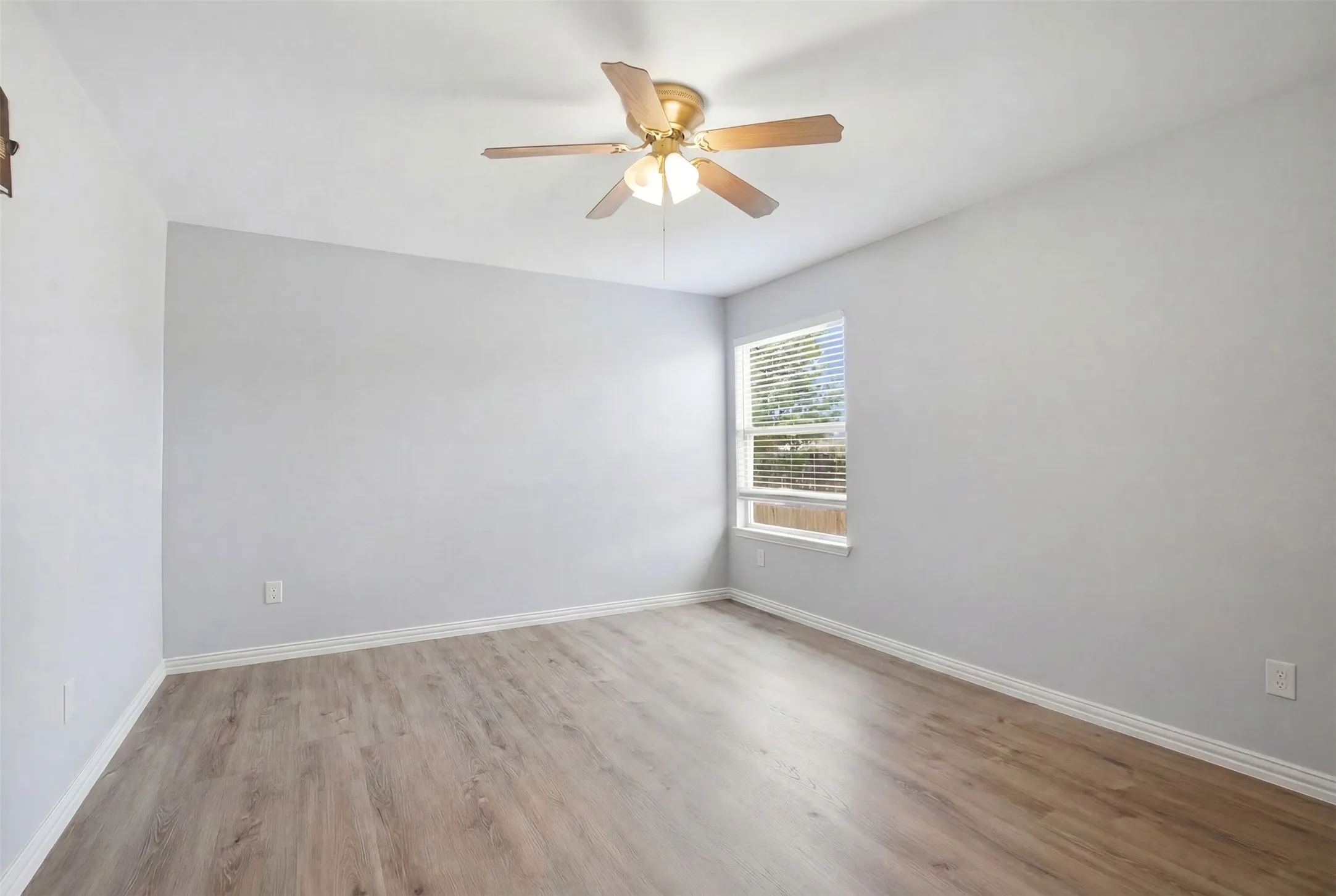 Spacious interior room with wood-finish flooring, light-toned walls, and a ceiling fan