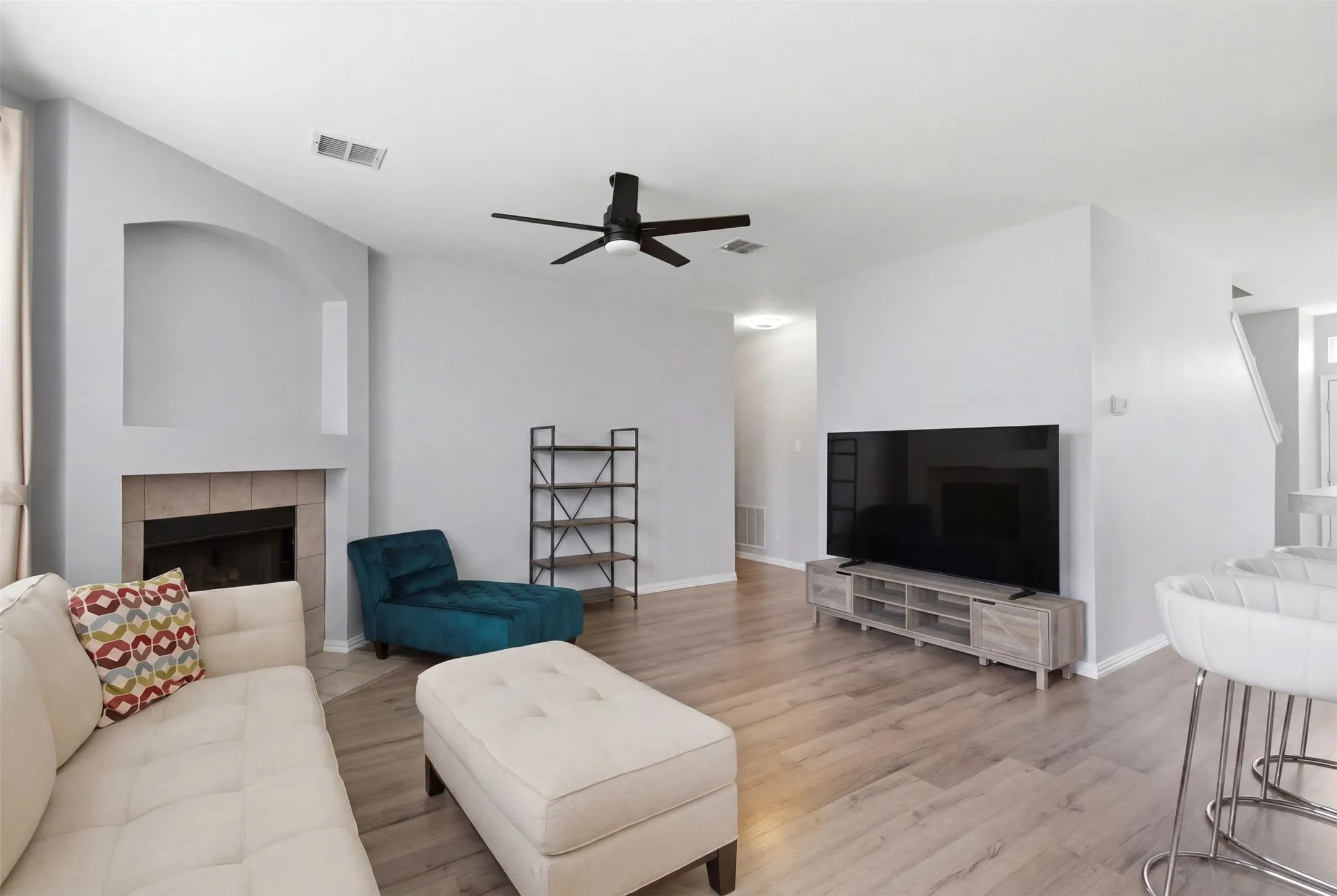 Spacious living area featuring wood-finish flooring, a tiled fireplace with an arched niche, and a ceiling fan