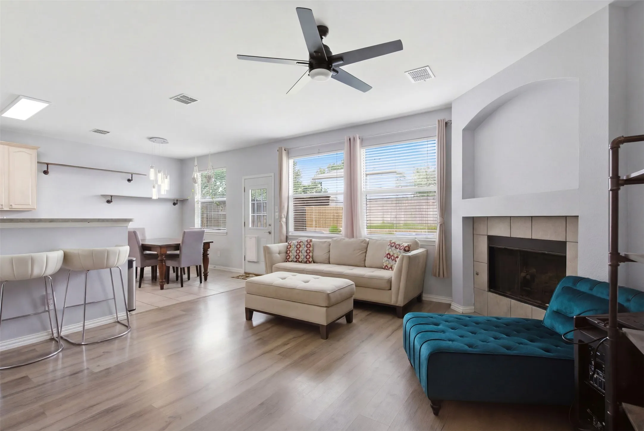 Spacious living area featuring wood-finish flooring, a tiled fireplace with an arched niche, and multiple windows