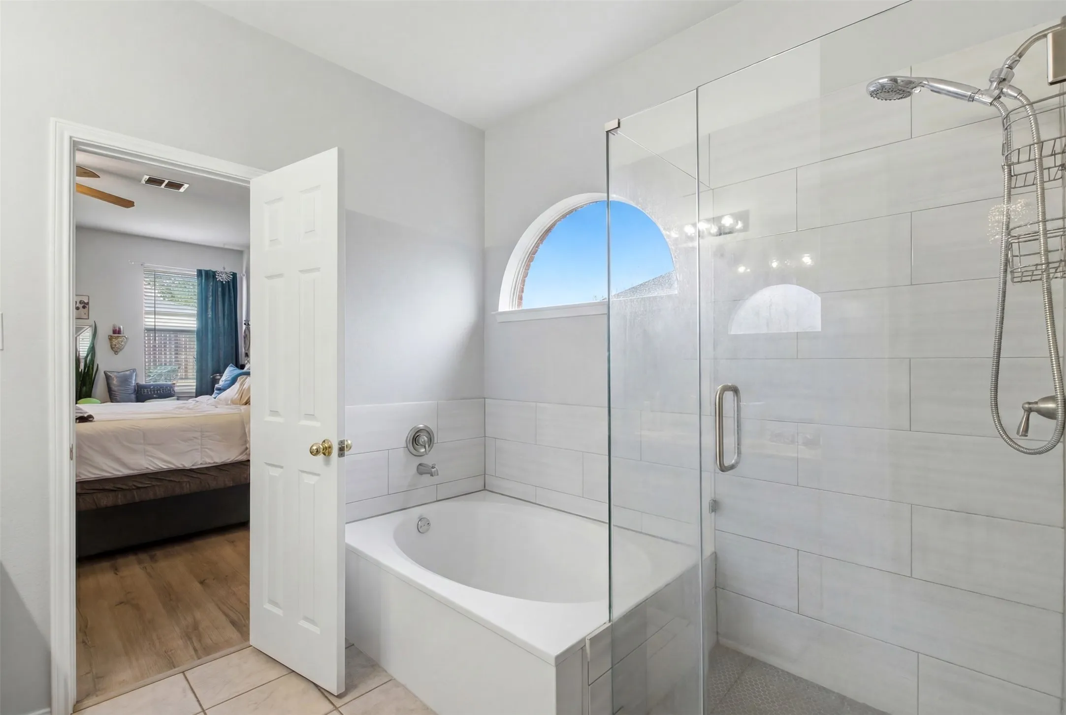 Bathroom with a glass-enclosed shower, built-in soaking tub, and an arched window