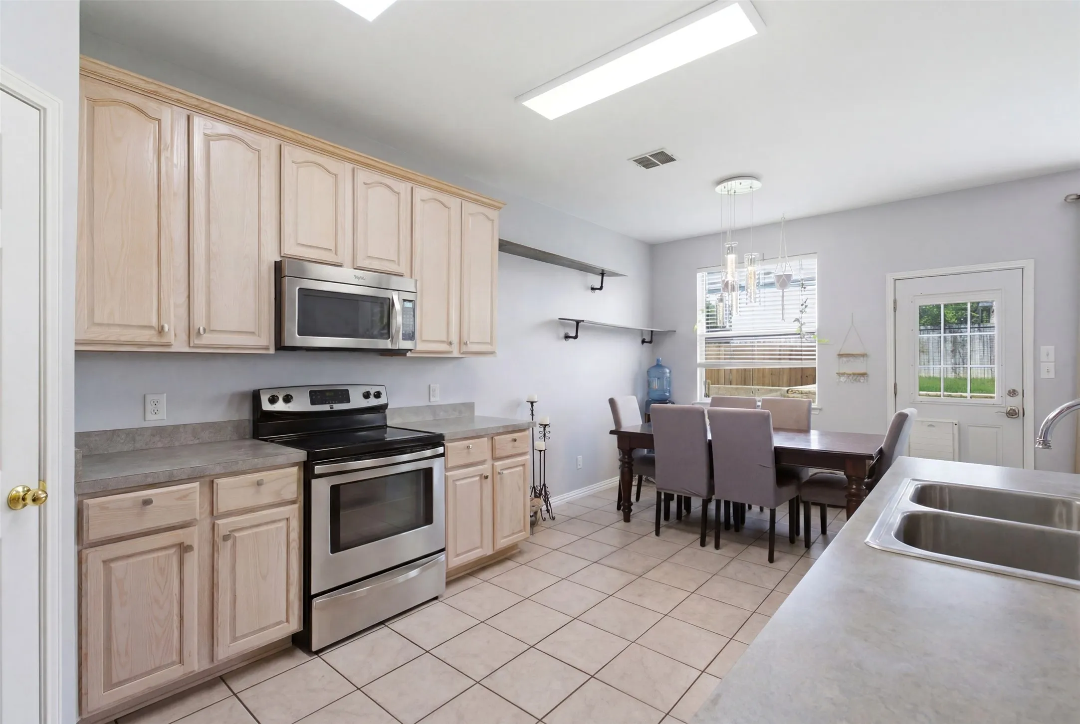 Kitchen featuring light wood-finish cabinetry, stainless steel appliances, and a double basin sink