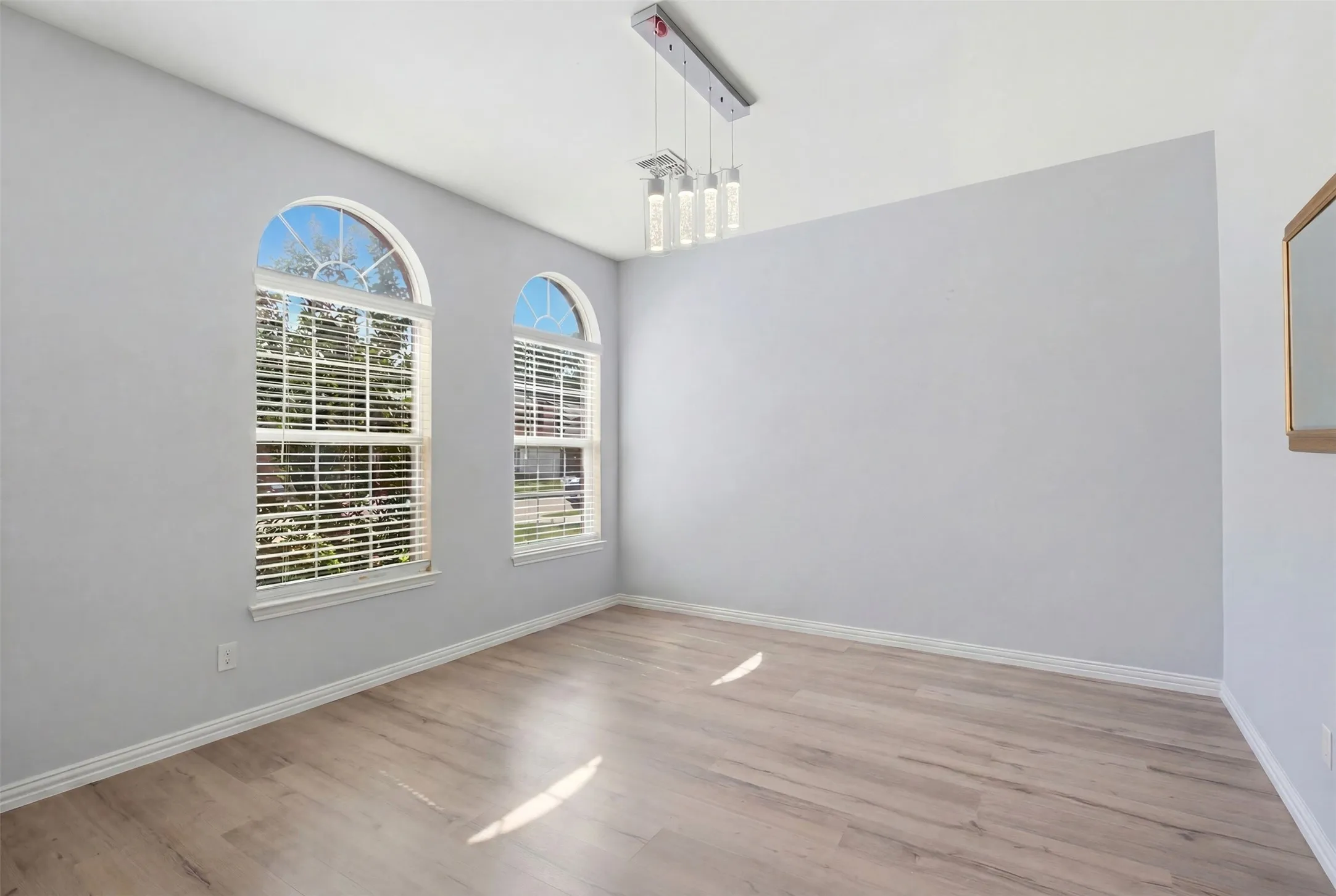 Bright room featuring two arched windows with blinds, wood-finish flooring, and a modern multi-pendant light fixture