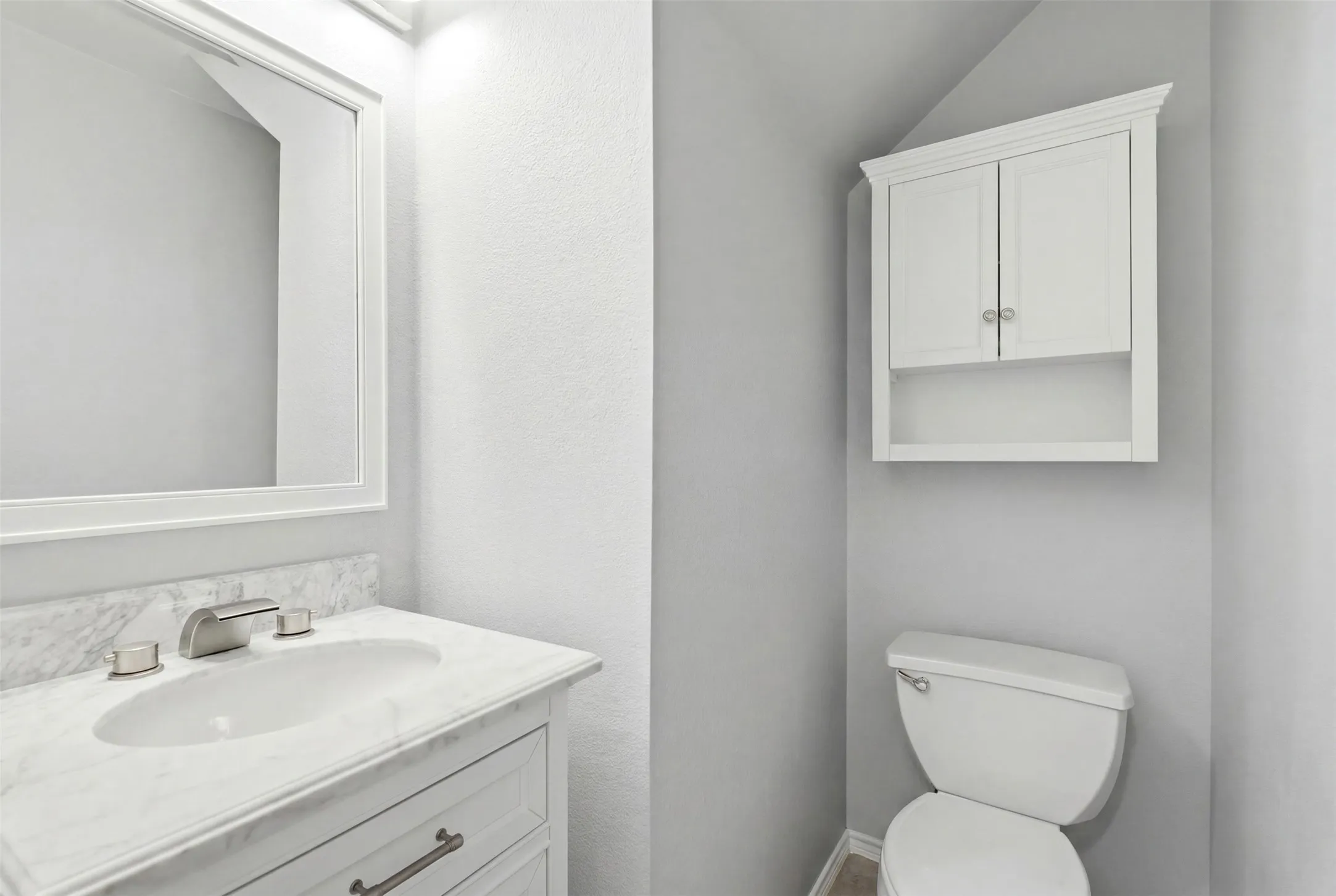 Bathroom featuring a white vanity with a rectangular undermount sink, a stone-finish countertop, and a framed mirror
