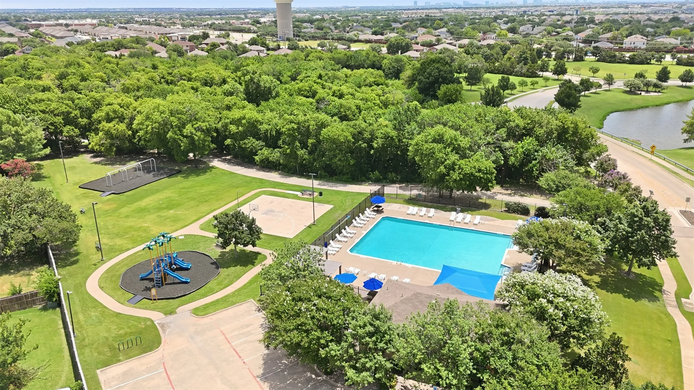 Community amenities featuring a swimming pool, shaded pool deck, playground area, sand volleyball court, and ample green space